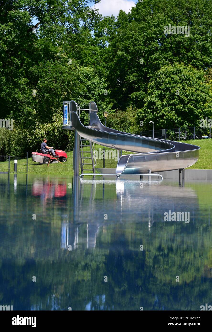 Kleinmachnow, Germany. 27th May, 2020. An employee of the open-air swimming pool Kiebitzberge mows the grass of a sunbathing area behind the non-swimmer pool with a lawnmower. In addition to the sports pool with 50-metre lanes, the pool has a large pool for non-swimmers and an extensive sunbathing area. The planned start of the season on 01.05.2020 had been postponed for the time being due to the regulation to contain the Corona pandemic. Credit: Soeren Stache/dpa-Zentralbild/ZB/dpa/Alamy Live News Stock Photo