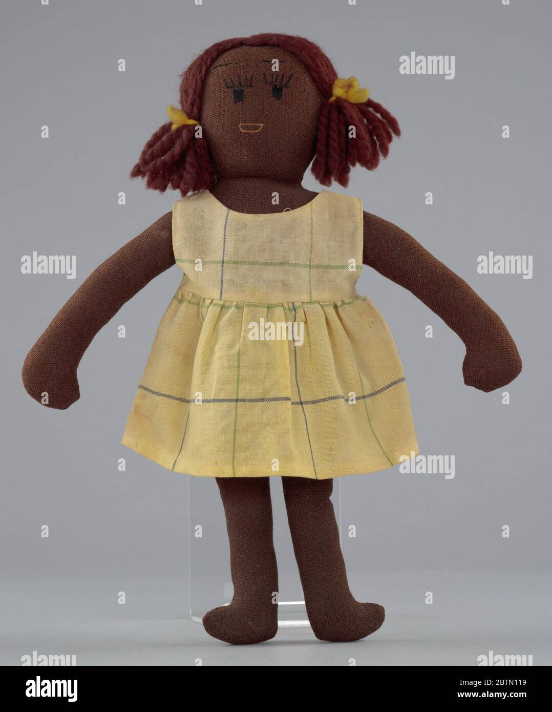 Female doll with tan clothing. A female cloth doll with tan clothing. The doll is wearing a tan dress with stripes. The doll's hair is in pigtails with cloth bows. Stock Photo