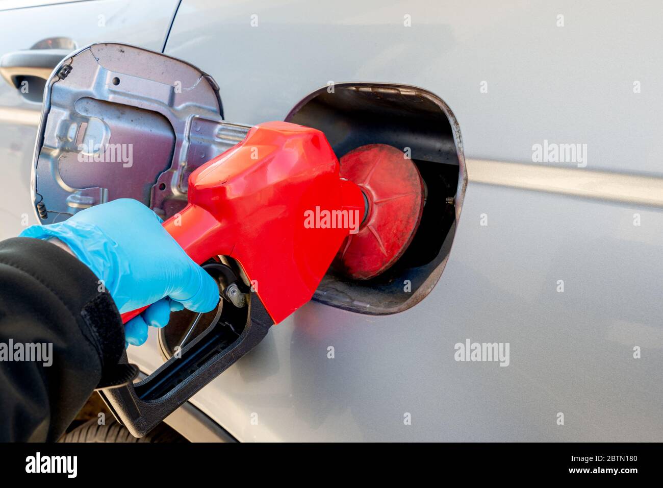 Hand wearing a blue personal protective glove pumps gas into an automobile. Shallow depth of field, focus on pump. Stock Photo