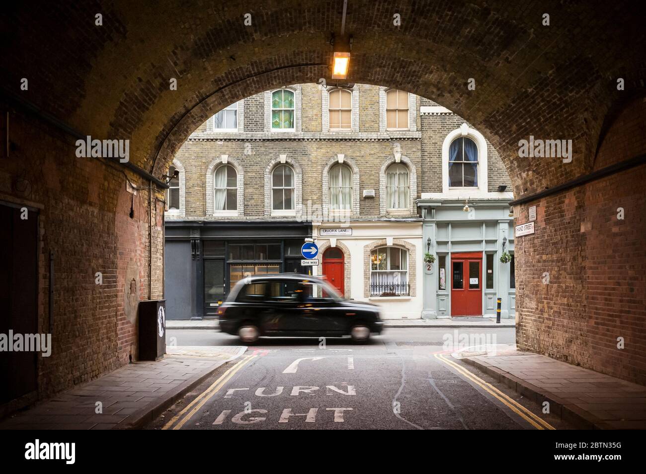 Traditional London black cab driving along Crucifix Lane in Borough, as seen through the railway arch of Shand Street, in Southwark, London SE1, Engla Stock Photo
