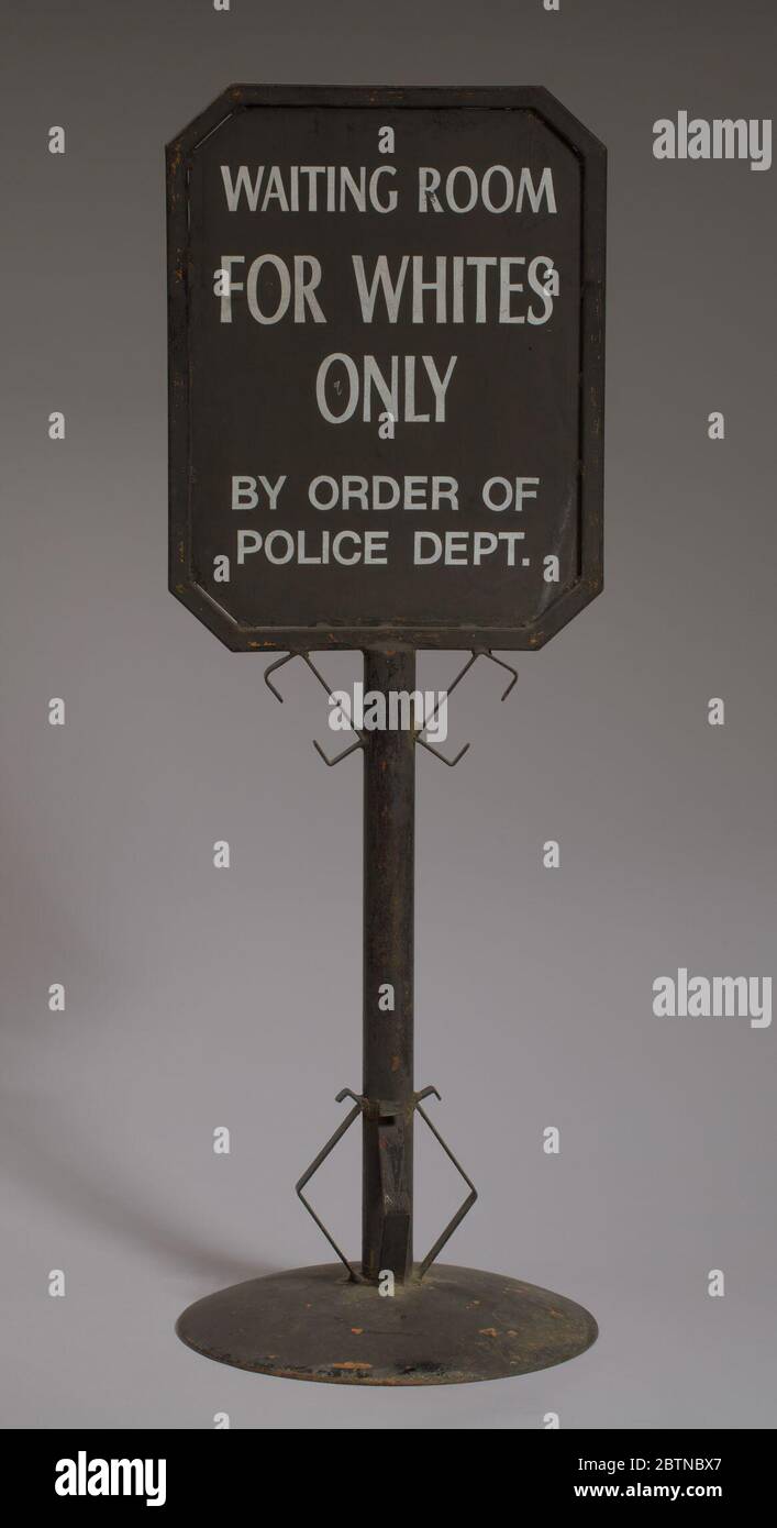 Sign from segregated railroad station. A metal double-sided black railroad sign that reads: [WAITING ROOM / FOR WHITES / ONLY / BY ORDER OF / POLICE DEPT.] in white paint. The writing is on a framed square plaque at the top of the sign. Stock Photo