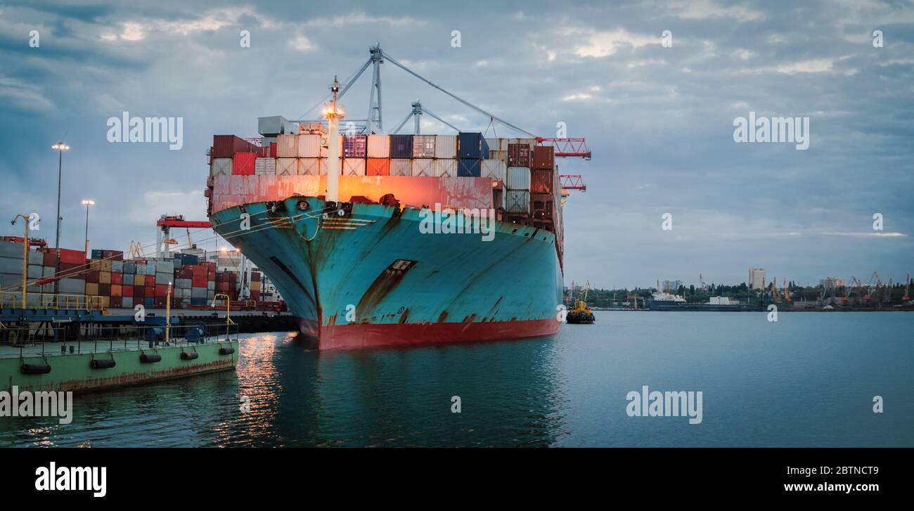 Container cargo ship load in the seaport at dusk. Logistics and transportation of Container Cargo ship with working crane bridge in shipyard, logistic Stock Photo
