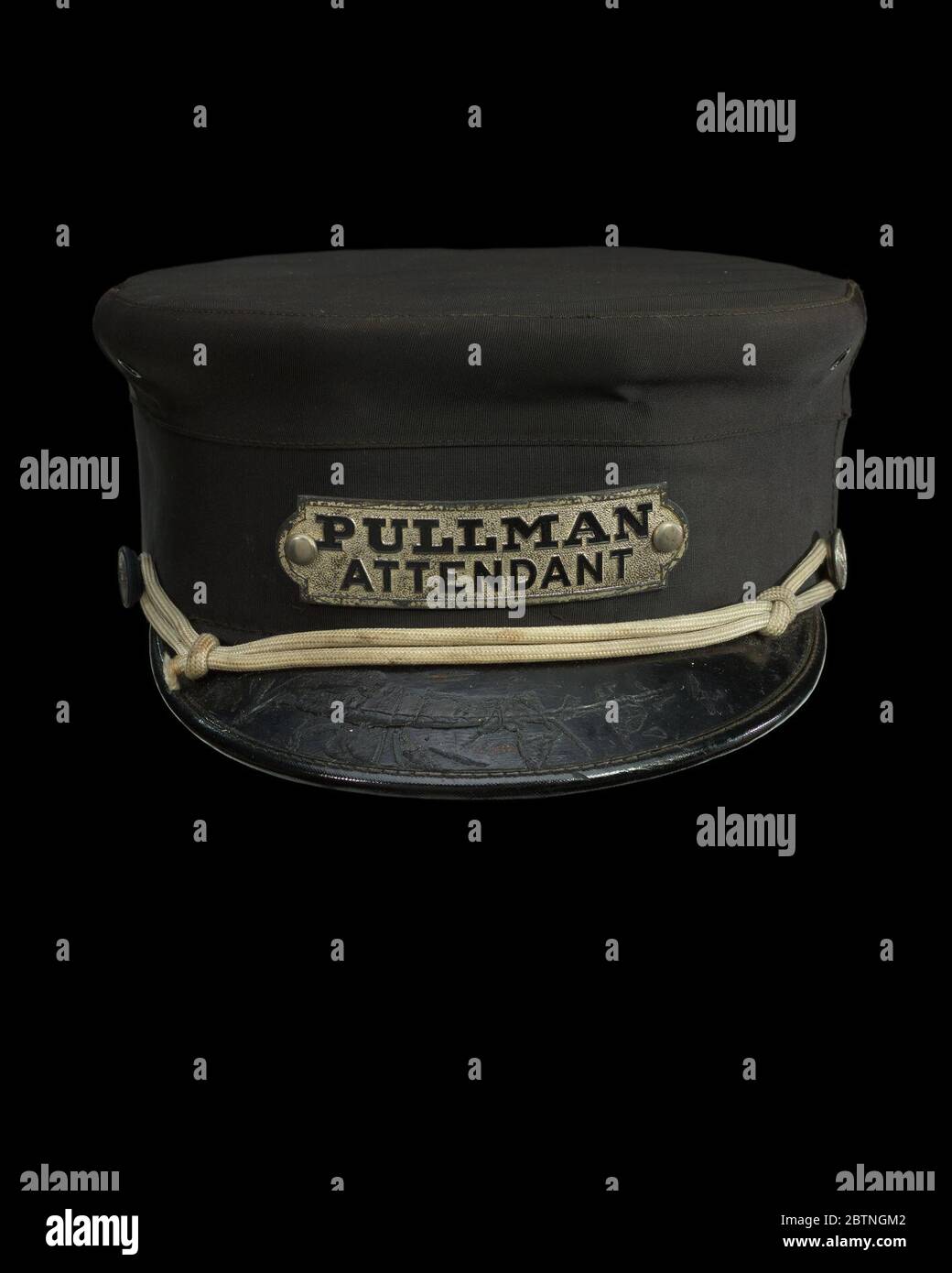 Uniform cap for a Pullman attendant. Uniform cap worn by attendants on Pullman railway cars. The hat is in the style of peaked cap with a leather brim. A cream colored cord wraps around the crown of the hat above the brim and has two knots on either side. The leather brim is extremely scratched. Stock Photo