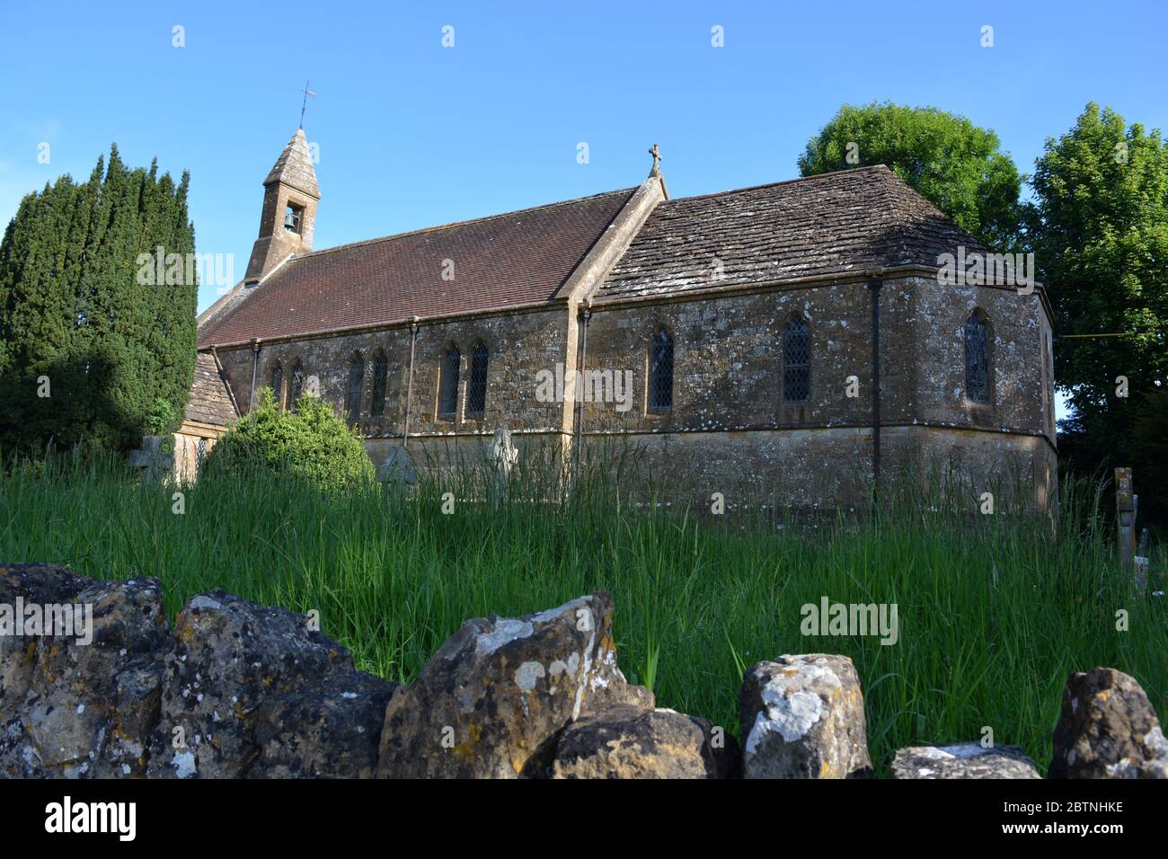 View over the boundary wall to Church of St Cuthbert, closed during the coronavirus pandemic, overgrown grass in the church graveyard. Oborne, Dorset Stock Photo