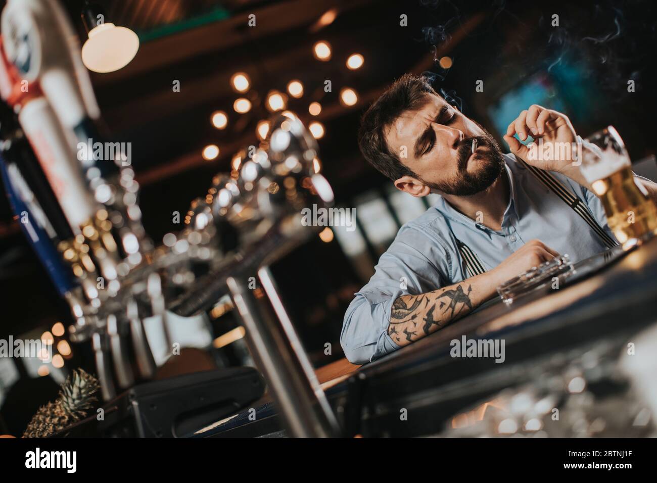 Young man drinking beer and smoking cigarette at pub in the night club ...
