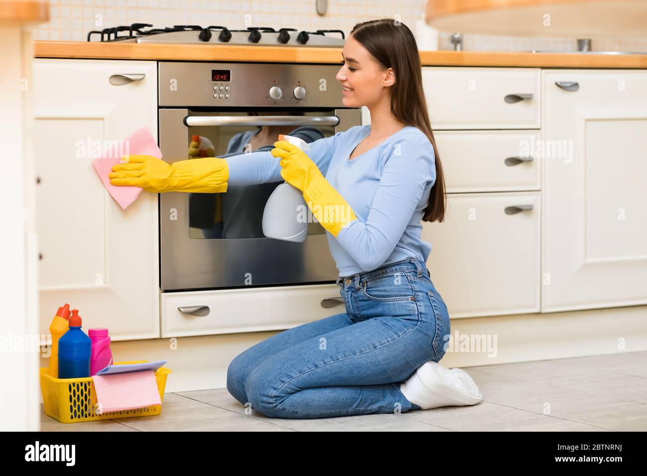 Young woman cleaning kitchen furniture using sprayer Stock Photo
