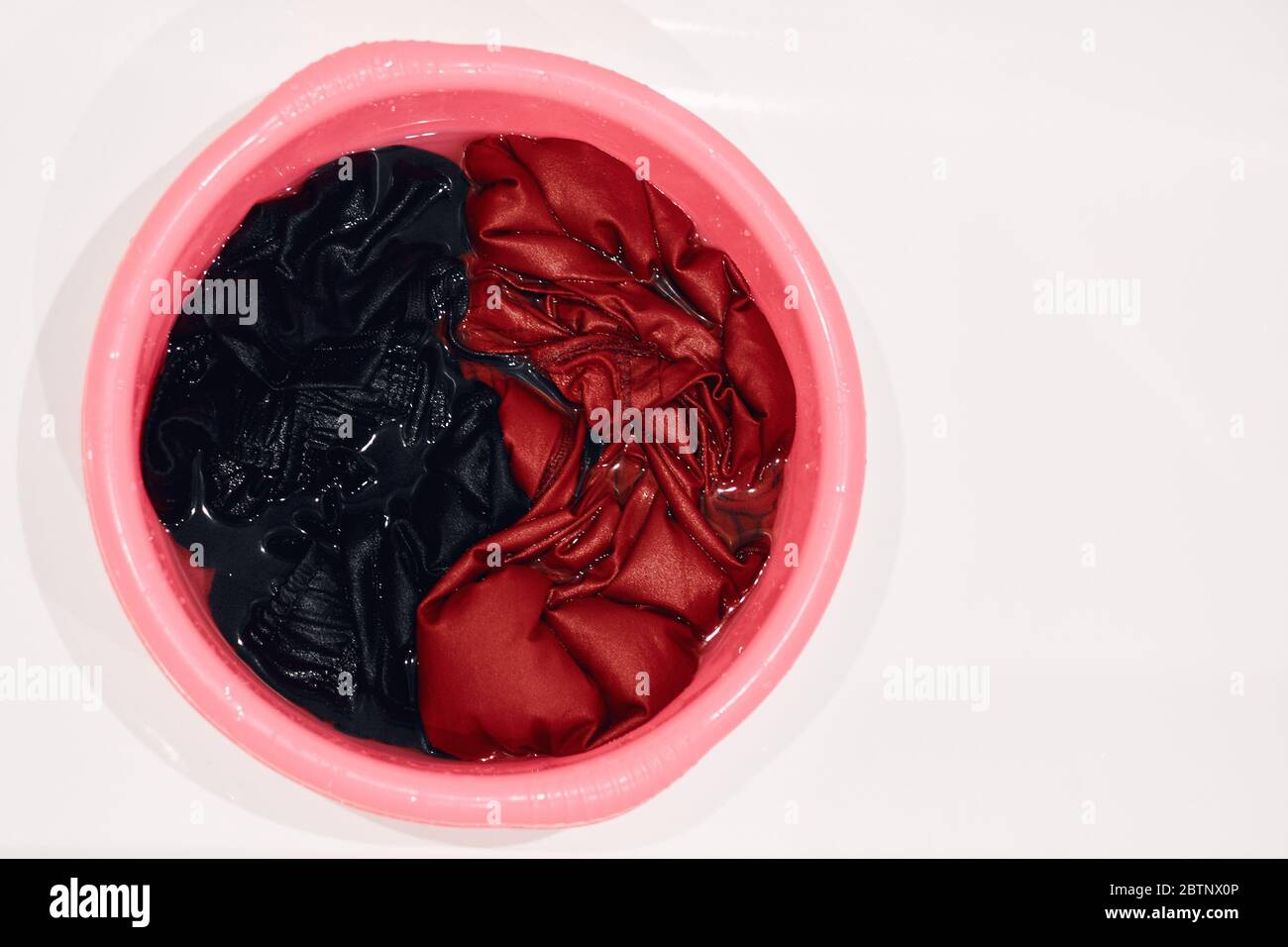 soaked dirty clothes in a red basin on a white bath. isolated Stock