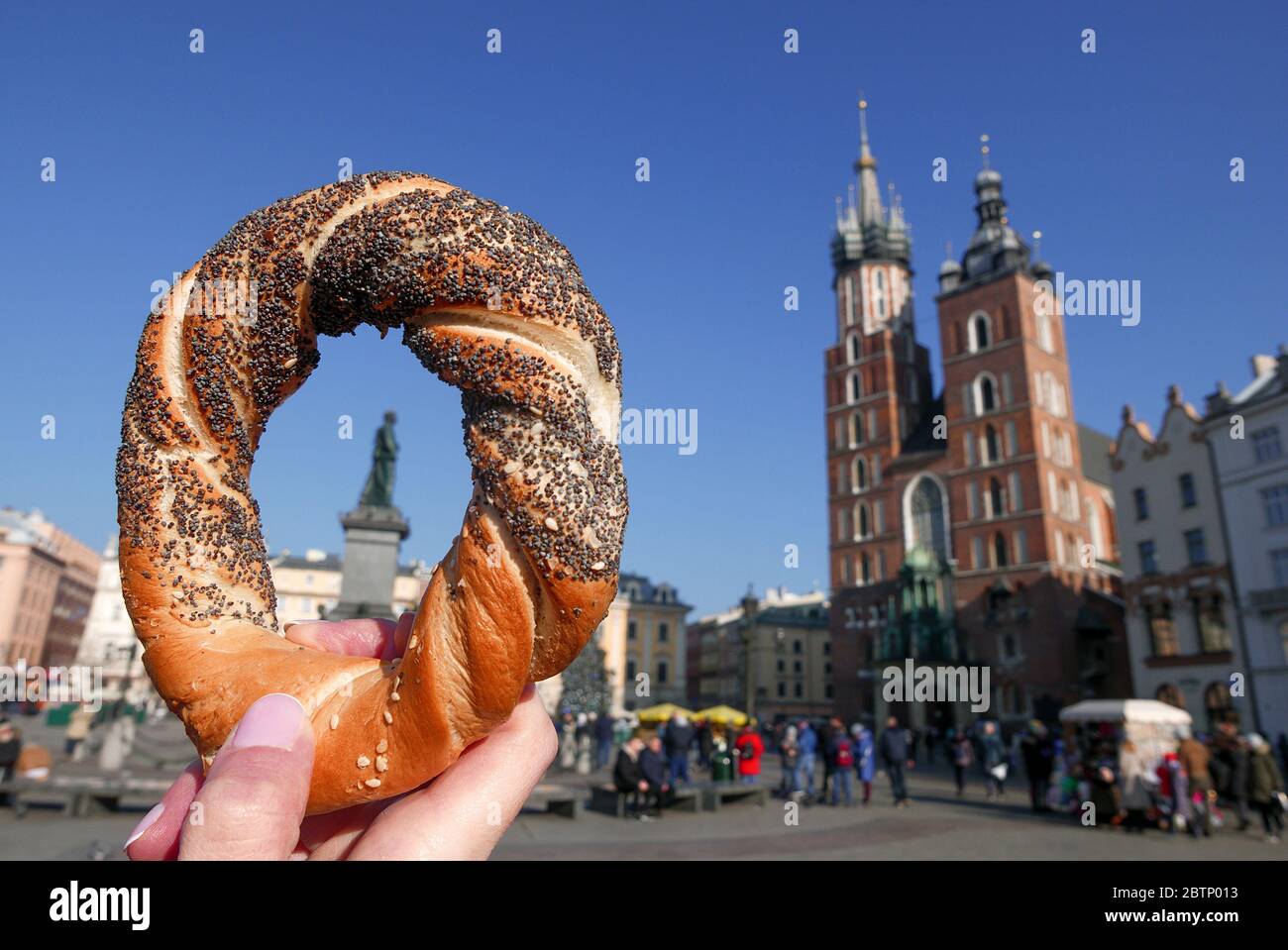 Woman hand holding bagel / obwarzanek, traditional polish snack. The Mariacka Tower in the background. Stock Photo
