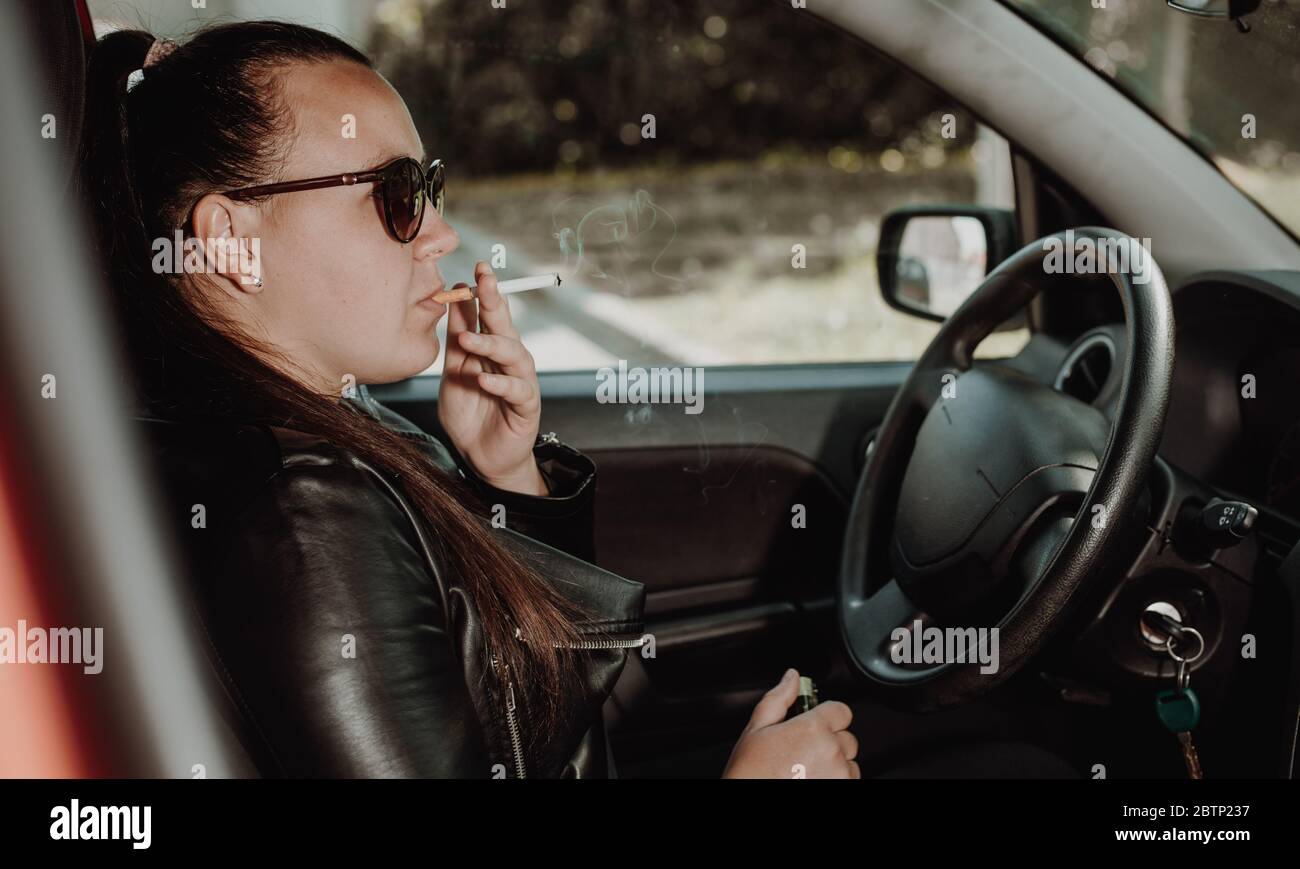 Young woman smoking a cigarette while driving a car, transportation