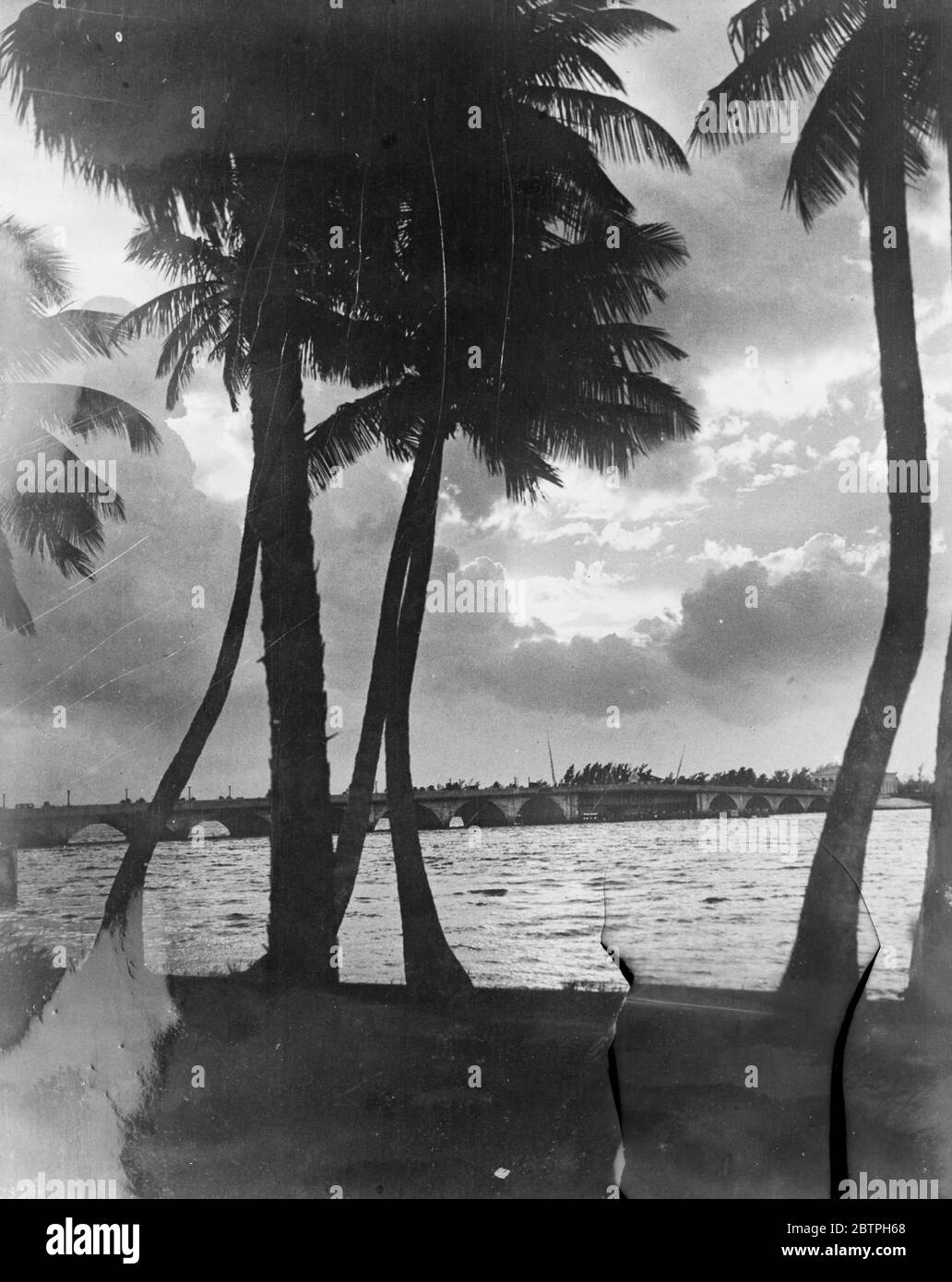 A Florida sunset . Breaking through the lowered clouds after a rainstorm , the setting sun creates this beautiful scene at Palm Beach , Florida . the bridge in the background separates Palm Beach from West Palm Beach . 23 January 1932 Stock Photo