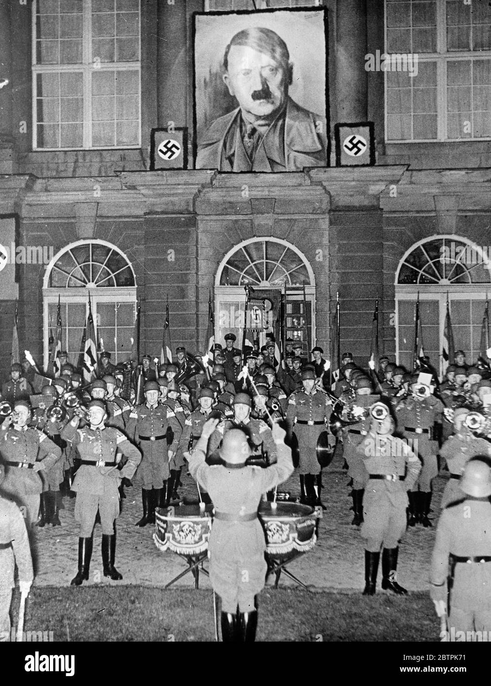 Victory serenade for Hitler . The band of the Goering regiment playing in front of the Charlottenberg Castle , near Berlin , in celebration of Hitler 's victory . A huge election portrait of the leader overshadows the scene . 30 March 1935 Stock Photo