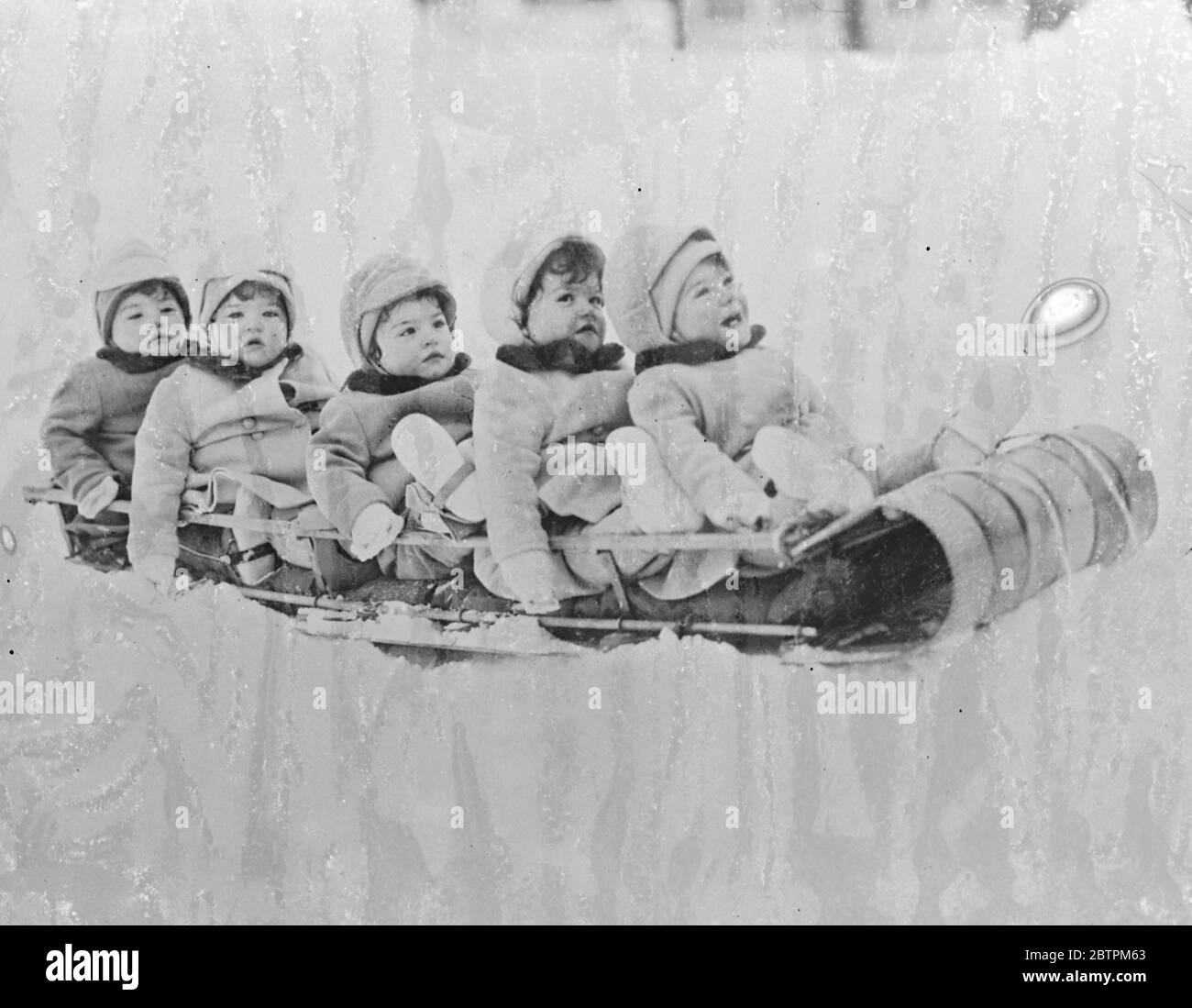 Quins go sledging . The Dionne Quintuplets had their first taste of the thrills of winter sport in the garden of their private hospital at Callender , Ontario , after several heavy snowfalls . Snugley wrapped up in their warm woollies , the Quins were taken for a sledge ride by Dr A B Dafoe , their own doctor , under watchful eyes of their nurses . Then they had a glorious romp in the snow which was something quite new to them . Photo shows , Marie trails her hand in the snow as she goes for a sledge ride with her sisters , left to right , Marie , Annette , Cecile , Yvonne and Emilie . 19 Apri Stock Photo