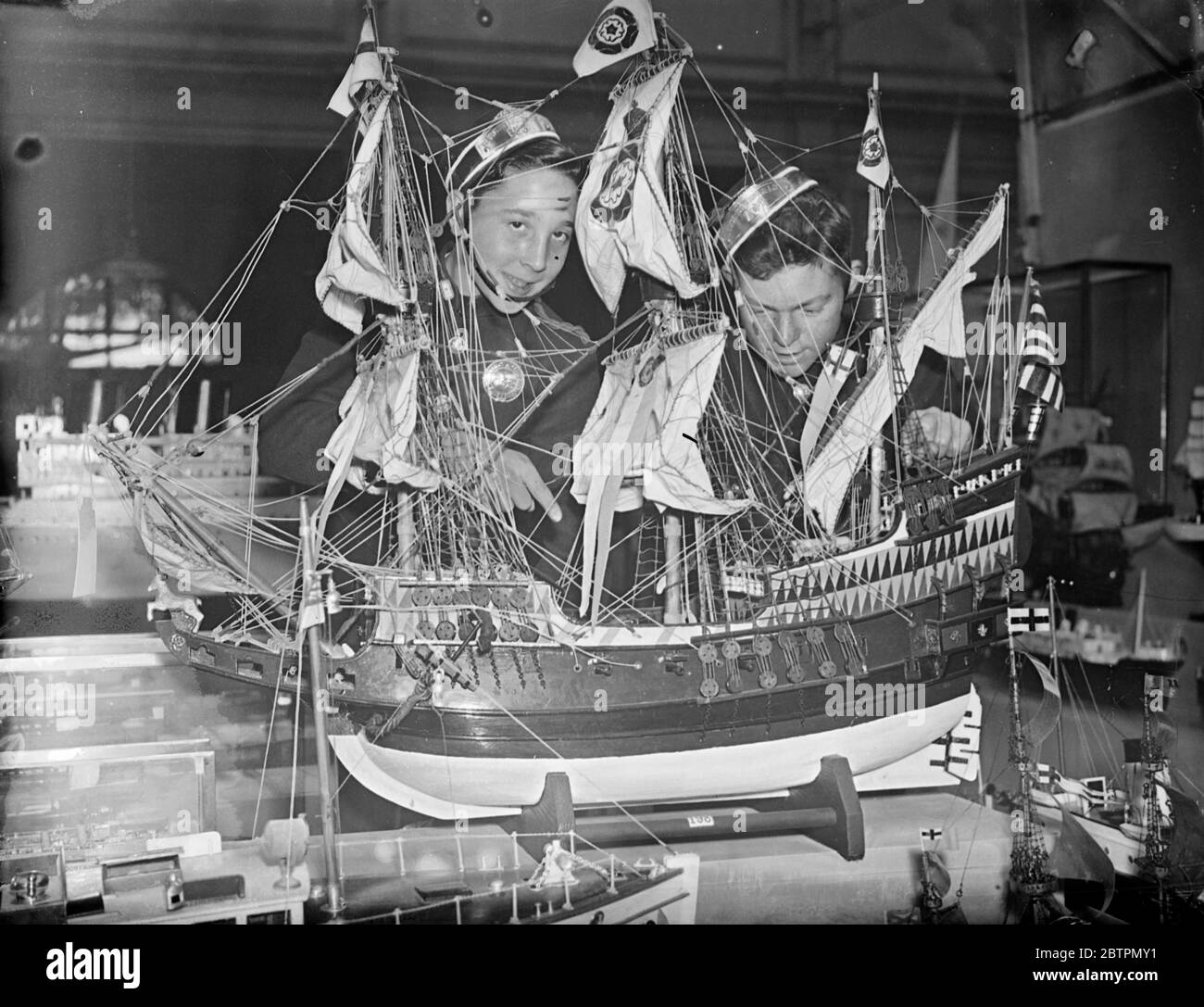 Model Engineering Exhibition opens. Youth and age have a mutual interest in the Model Engineering Exhibition which has opened at the Horticultural Hall, Westminster, London. The model makers, also have gone back many years in history for their inspiration and miniatures of Drake's Golden Hind stand side-by-side with the latest type cabin cruisers and warships. Photo shows: messenger boys inspecting a model of Drake's Golden Hind at the exhibition. 17 September 1936 Stock Photo