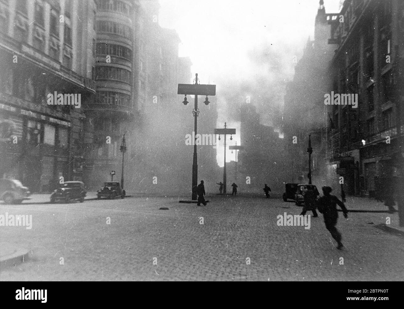 Madrid again under fire. Shell that killed three, injured 15. British women MPs in danger. This picture just received in London from Madrid, was taken by photographer in an ambulance as rebel bombs and shells rained down in the intense bombardment which the rebels are again directing on the city. People can be seen running for their lives in the Gran Via, Madrid street, as a shell hits a building on the right. This shell killed three persons and injured 15. The people running in the centre were caught by the explosion and badly hurt. This bombardment also endangered the lives of the Duchess of Stock Photo
