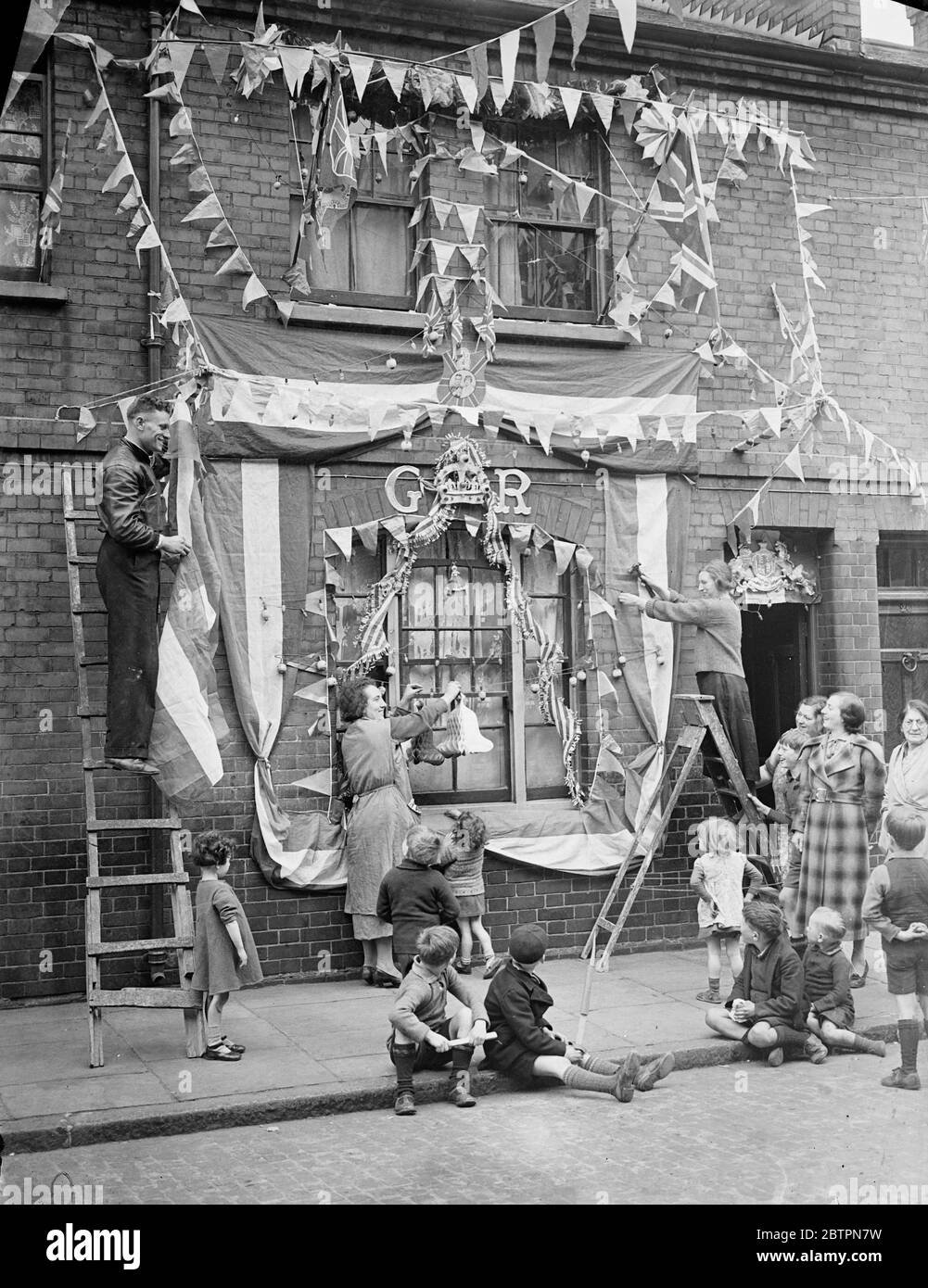 Coronation House Gathering funds by door-to-door collections, many of the poorest streets in the East End of London have rivalled the West End with the brilliance and variety of their decorations for the Coronation. Photo shows: fixing the Coronation decorations to a house in Campbell Street Bethnal Green. 7 May 1937 Stock Photo