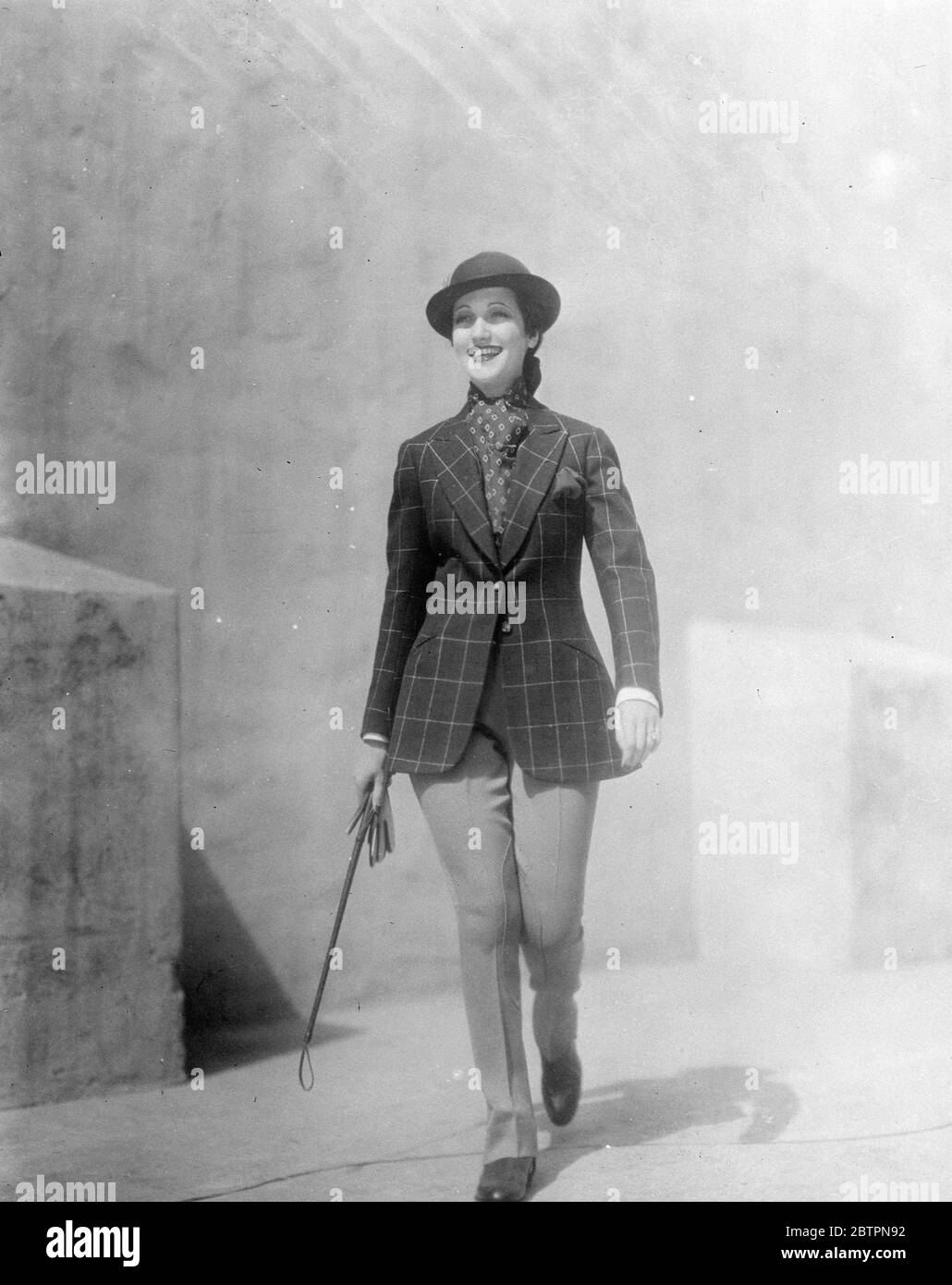 Fashion goes riding. Even Hollywood, birthplace of fashion, stared when Dorothy Lamour, the film actress, appeared in this ultra-smart tailored riding habit of wide-checked material to take her usual morning canter. A cravat with neat diamond pattern completes her costume. 5 June 1937 Stock Photo