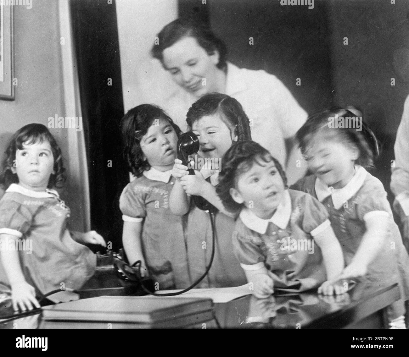 Quin makes a good listener. Dark haired Emilie, with a shy smile, listens intently to the voice of the Dionne quintuplets' own doctor, Allan Defoe, on the nursery phone at Callander, Ontario, Dr Defoe makes a special point of calling the quintuplets each day by telephone. 13 June 1937 Stock Photo
