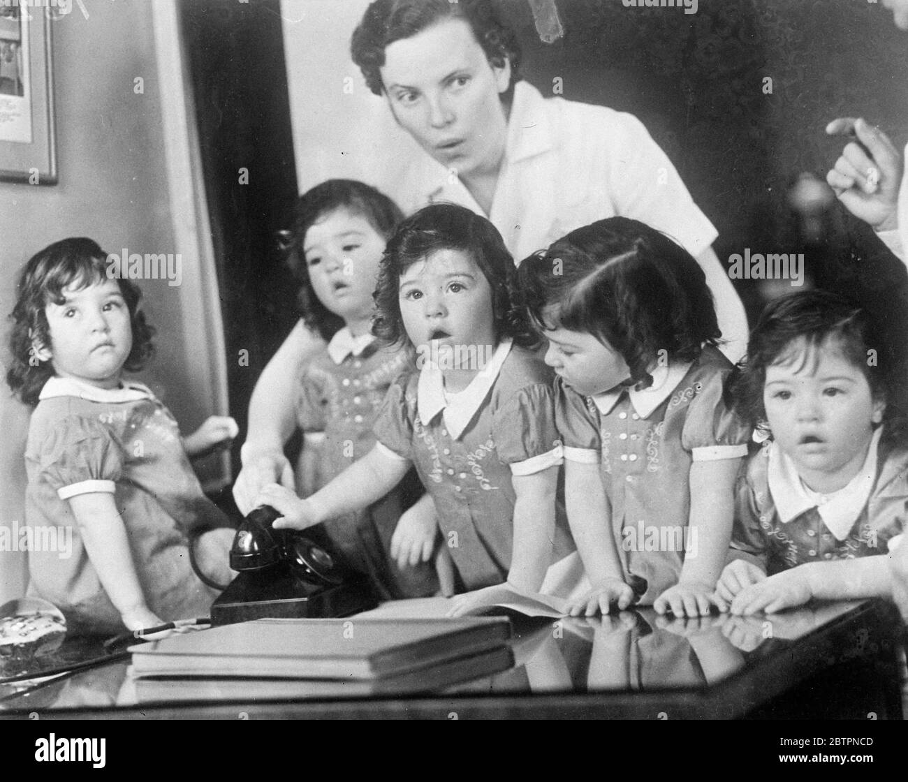 Quin makes a good listener. Photo shows: Dionne quintuplet talking to their own doctor, Allan Defoe, on the nursery phone at Callander, Ontario. Dr Defoe makes a special point of calling the quintuplets each day by telephone. 13 June 1937 Stock Photo