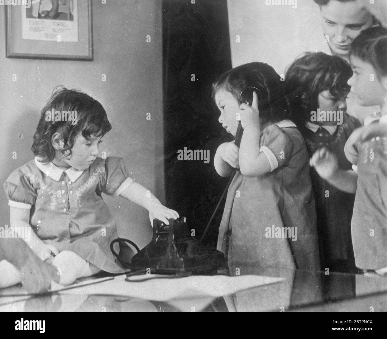 Quin makes a good listener. Photo shows: Dionne quintuplets talking to their own doctor, Allan Defoe, on the nursery phone at Callander, Ontario. Dr Defoe makes a special point of calling the quintuplets each day by telephone. 13 June 1937 Stock Photo