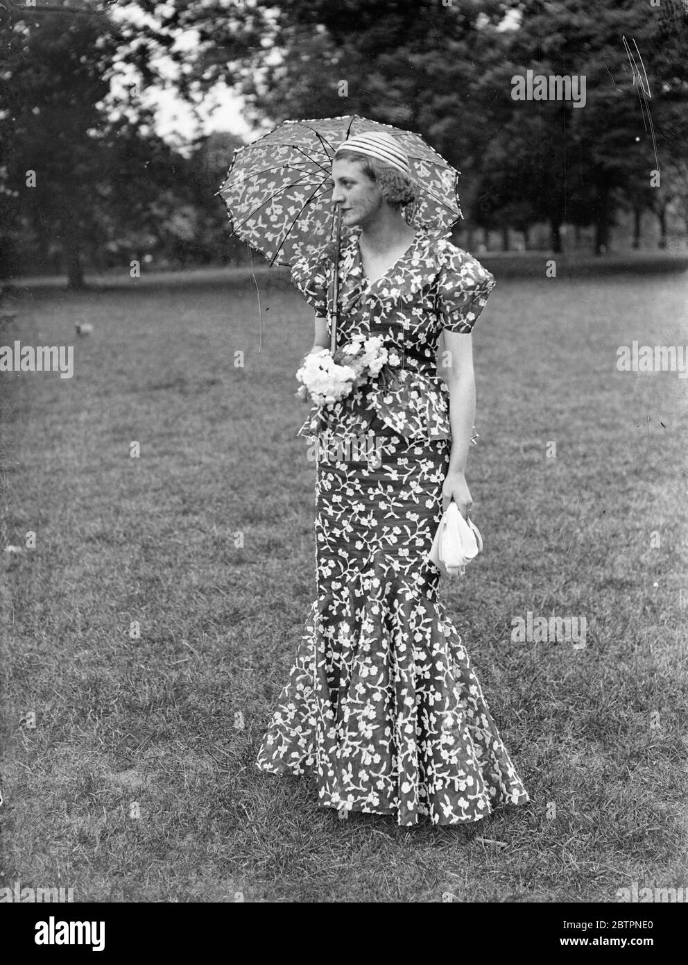 Prepared for a sunny Ascot. A flowered fashion of navy blue wall, embroidered organdia, with parasol to match, which will be seen on the course when the Royal ascot opens next week Dress is trimmed with white violets. 11 June 1937 Stock Photo