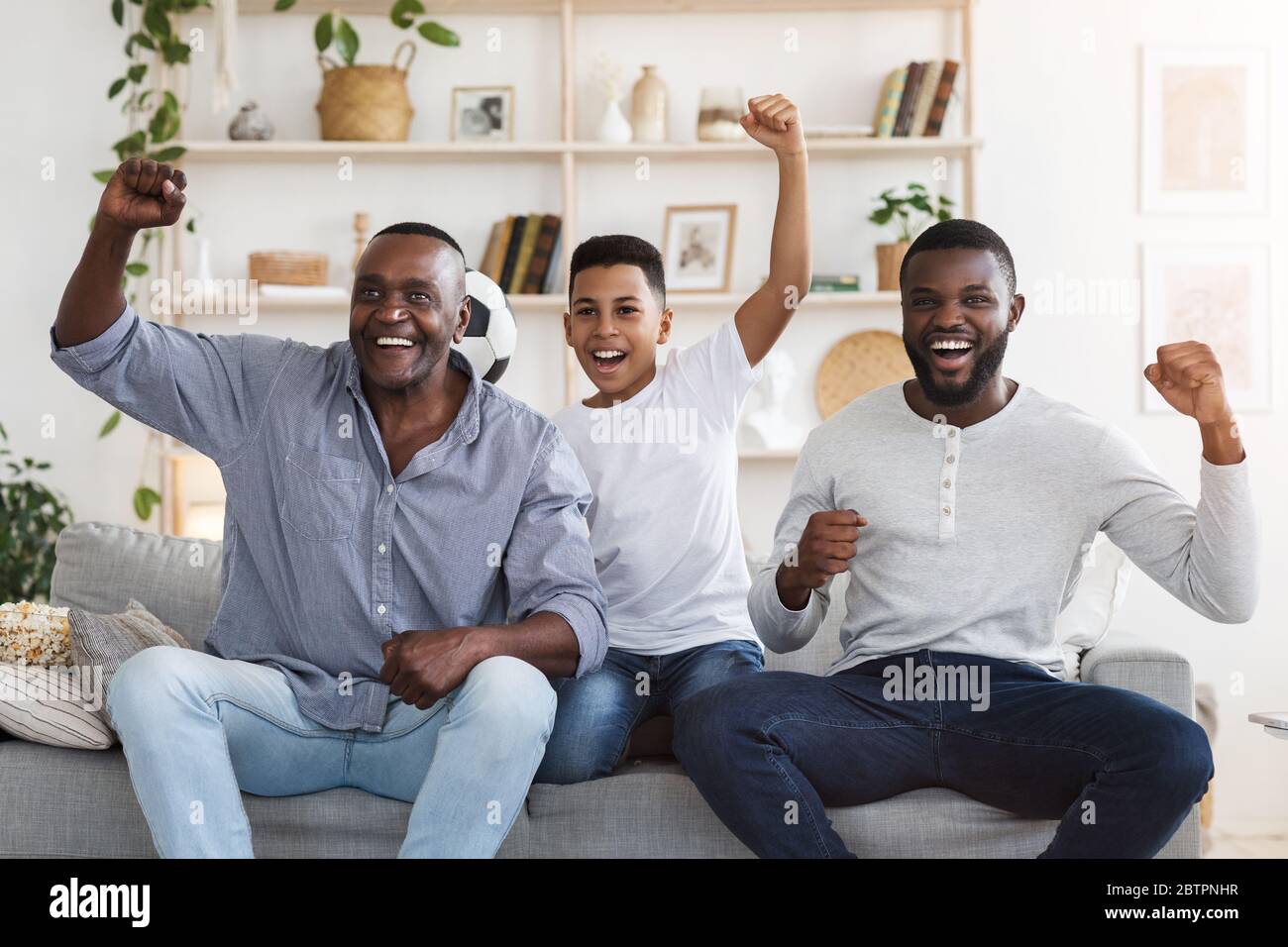 Soccer Fans. African Father, Son And Grandfather Watching Football Game On TV Stock Photo