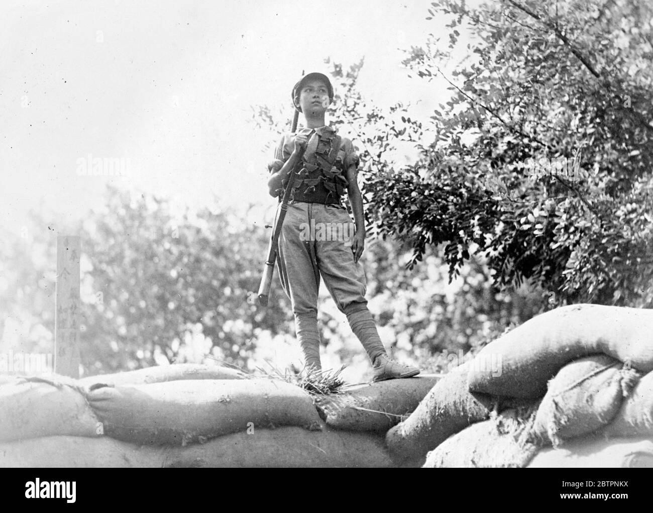 Girl soldier on the watch. China's fighting women defend their home. Centuries of grim struggle against adversity, of fighting against her, implacable enemy-nature-has fitted China's womanhood for the greatest battle-with the invading Japanese forces now menacing the entire nation. Women, their only uniform, a tattered shirt, trousers and, have joined China's non-descript armies around Shanghai in the North. Photo shows, a girl soldier, a rifle slung across the shoulder, keeping watch for a pile sandbags north of Shanghai. Stock Photo