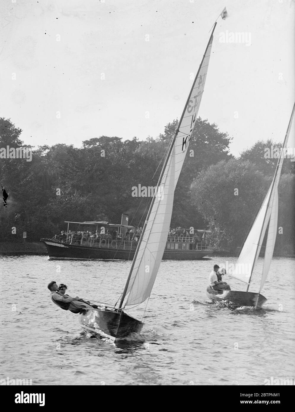Yachting girls race in Teddington. Yachting girls, sailing, 14 feet international class craft, competed in the ladies race of the Tamesis Club races on the Thames at Teddington today (Sunday). Photo shows, a yacht healing over during the ladies race. In the background. A river steamer can be seen passing the race. 26 September 1937 Stock Photo