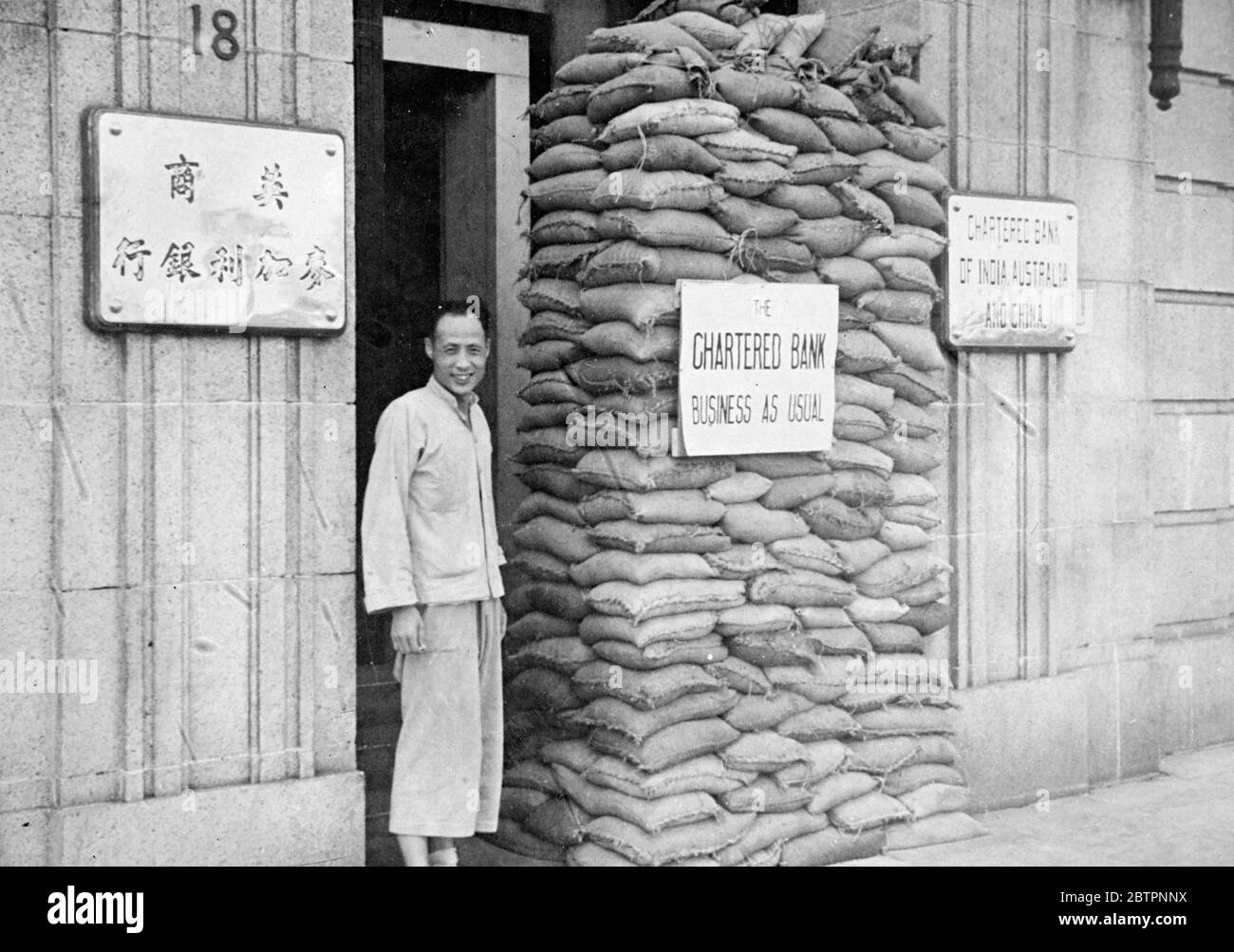 Banking with sandbags. Business as usual in Shanghai. Though Shanghai's trade has been almost ruined by the disastrous Sino- Japanese war, some businesses housed along the Bund (waterfront) have sandbagged windows and doorways as protection against flying shrapnel and bullets and are endeavouring to carry on as usual. The buildings on the Bund , not only in danger by fire from Japanese warships in the Whangpoo river, but also by Chinese firing from Pootung, across the river. Photo shows, the sandbagged doorway of a bank on the Bund at Shanghai, with a business as usual notic on display. 27 Sep Stock Photo