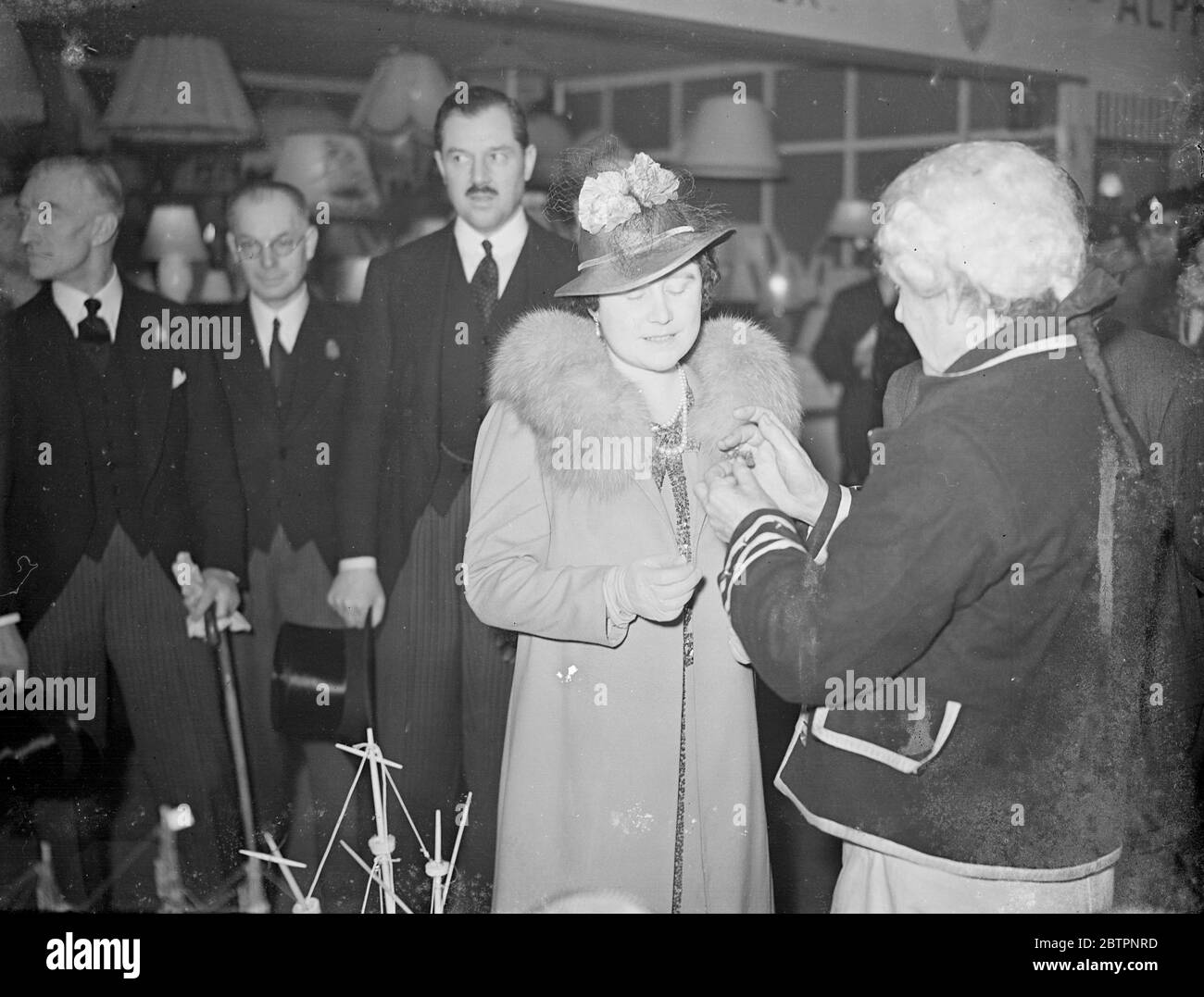 Queen and Queen Mary, talk with old Crossman at Olympia BIF. The Queen and Queen Mary again, visited the Olympia section of the British Industries Fair, and displayed great interest in the exhibits. Photo shows, the Queen watching Mr F A Saunders, aged 73, making models of old times ships at the stand of Messrs S J Lethbridge. 24 February 1938 Stock Photo