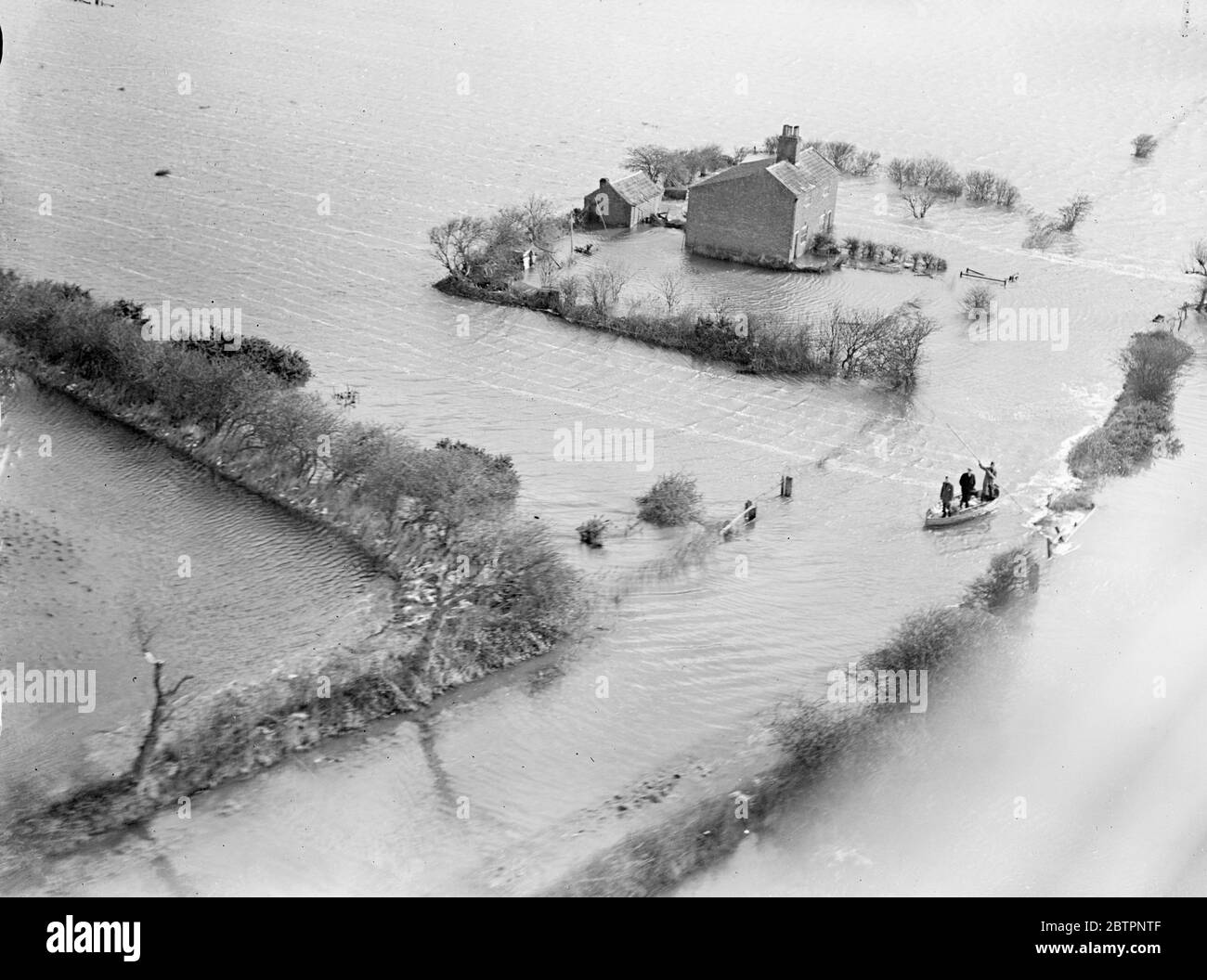 Pictures by special plane. The sea sweeps over East Norfolk. A new crisis caused by the maximum spring tide faced the flooded villages in the Horsey area of Norfolk today (Monday). The villages were flooded when the Gale lashed sea burst coast defences and swept inland covering 20 mi.Â². The sea forced a gap three miles long, believed to be the biggest made in East Norfolk for 50 years, and compelled 150 inhabitants of Horsey to leave their homes. Photo shows, people being rescued by boat from I'm a ruined farmhouse near Horsey.. 14 February 1938 Stock Photo