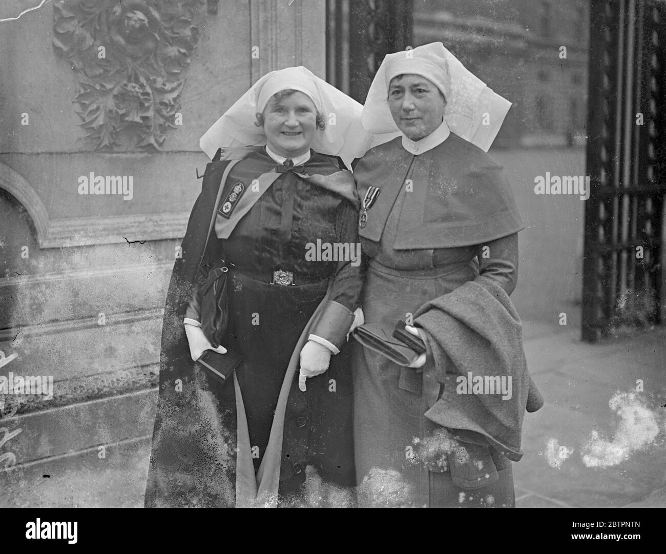 Nurses at Kings investiture. Honours awarded in the New Year's Honours List were conferred by the King at an Investiture in Buckingham Palace, London. Photo shows, two nurses and leaving out the investiture. They are, sister, Mary, Penelope d'Exeter Jordan of her HMS 'Caledonia', training ship and superintending sister of Queen Alexandra's Royal Naval Nursing Service, and Sister Margaret Bremner of Queen Alexandra's Indian Medical Service. They received a Royal Red Cross order. 15 February 1938 Stock Photo