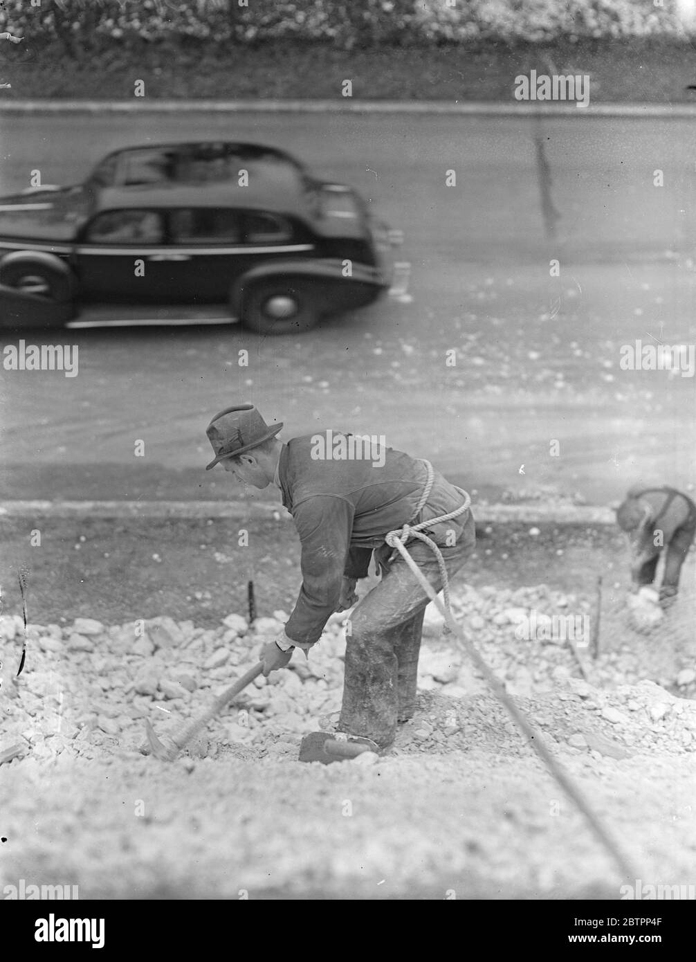 Surrey mountaineer!. Workmen, with safety ropes coiled around their waists, removing crumbling chalk, but is a danger to motorists, on the tall embankment. Flanking the Guildford bypass road, Surrey. 27 January 1938 Stock Photo