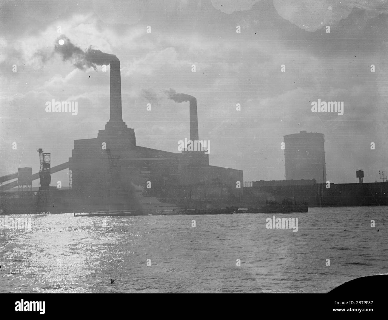 Dark giants of power!. Towering, graceful stacks of the Battersea Power Station with the streamers of smoke belching against a cloudy sky, cranes, and tugs puffing by on the sun sparkled river give an impression of the 'industrial Thames' source of London's power and wealth. 28 January 1938 Stock Photo