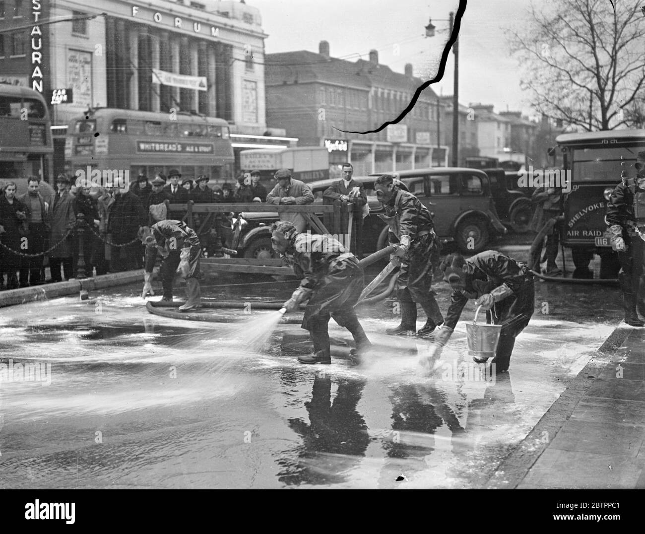 Ealings anti-gas squads at work. Watched by an interested crowd and with traffic passing by in the main road, volunteer members of the Ealing Councils anti-air raid squad demonstrated anti-gas methods outside the Town Hall at Ealing, London. Photo shows the squad, wearing masks and special suits, decontaminating an area outside the Ealing Town Hall , where a 'mustard gas bomb' has fallen,. 1 February 1938 Stock Photo