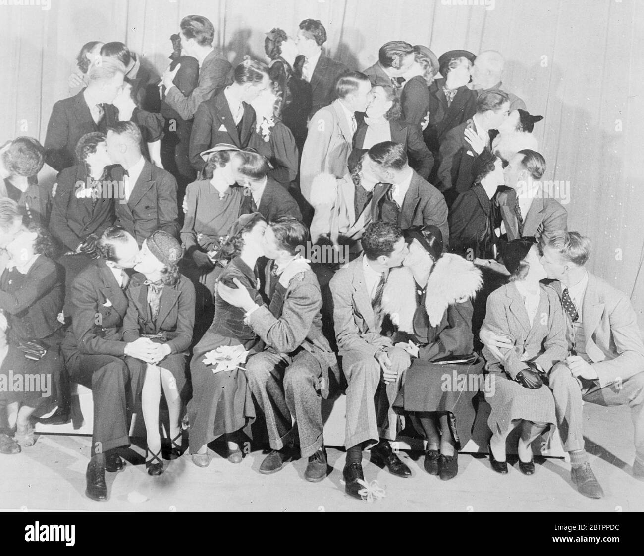 Kissing time!. In connection with a new radio play 'First Love', Rosalind Russell and James Stewart, the film actors, selected 100 engaged couples to attend the broadcast at the Los Angeles radio station. The couples were selected from the 'marriage'columns of Los Angeles newspapers. Photo shows, Rosalind Russell and James Stewart (centre, first row) gives some first-hand instruction in the proper close-up technique for an embrace, at the Los Angeles studio. Stock Photo