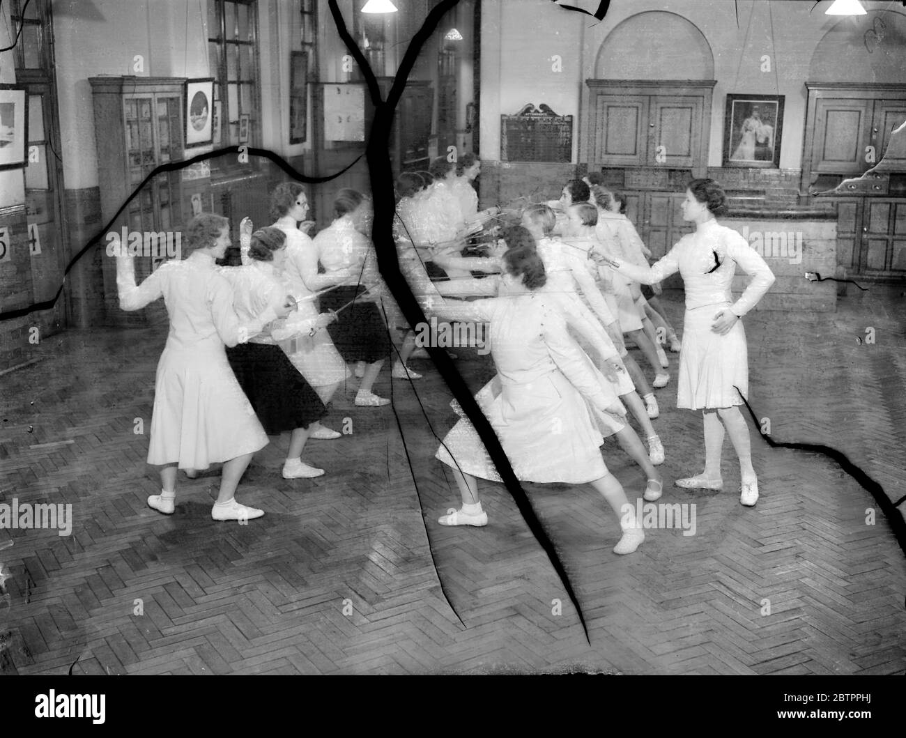 East End girls 'En Garde!'. Working girls of the East End of London are learning to fence at the London County Council's Fairclough Institute in Berner Street, Commercial Road. Under the direction of Miss Eleanor MacDonald, the young fencing expert who is acting as an instructor, the sport is gaining in popularity in the East End, where girls recognise its value as an aid to fitness and grace of figure. Photo shows, a class of girl fencers under instruction by Miss Eleanor MacDonald, at Fairclough Institute. 1 February 1938 Stock Photo