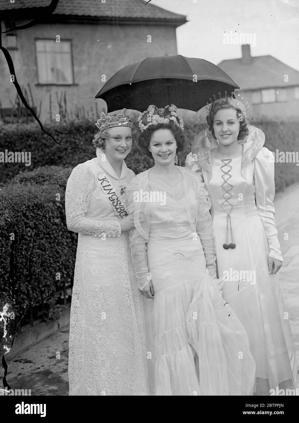 Carnival queens share an umbrella. Despite rain, large crowds watched the Carnival Processions pass through the streets of Wembley. Three Carnival Queens, of Wembley, Kingsbury and Kenton, were in the procession. Photo shows, the three Carnival Queens sheltering under an umbrella while waiting for the start of the procession, left to right, Trudie Deller (Kingsbury), Peggy Webb (Wembley) and Pamela Wainwright (Kenton). 16 July 1938 Stock Photo