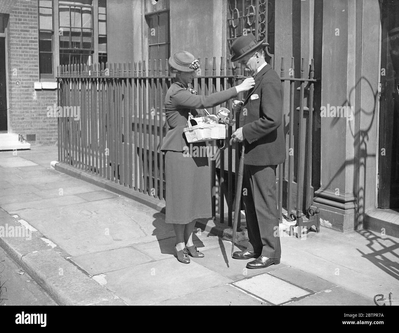 Premier biases Alexandra Rose. Mr Neville Chamberlain, the Prime Minister, was among the thousands of Londoners who bought an Alexandra Rose, a aid the hospitals. Photo shows, Mr Neville Chamberlain, buying an Alexandra Rose from Miss Ursula Lepine as he left 10 Downing Street. 23 June 1937 Stock Photo