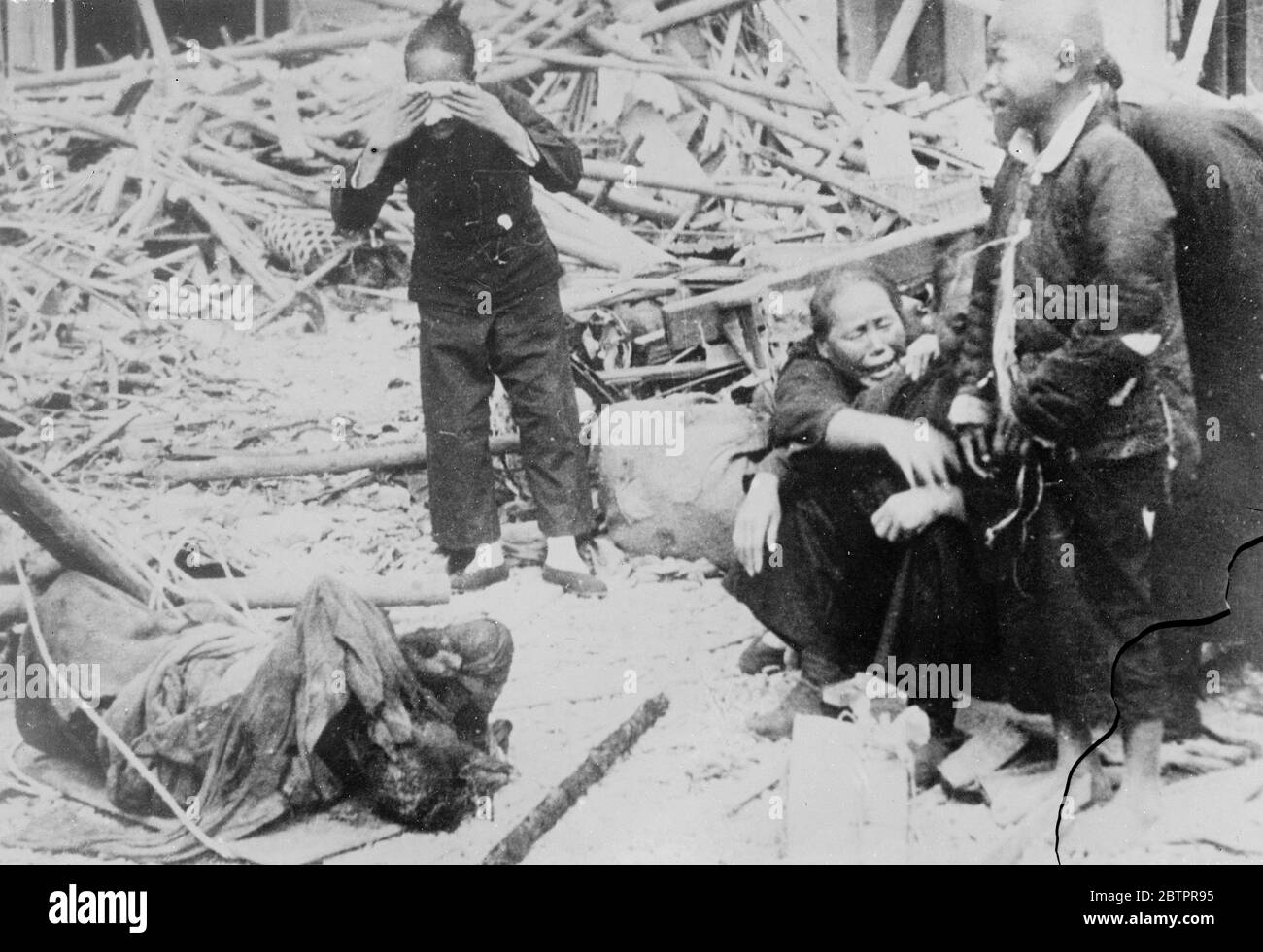 Just another death. But the world has crashed!. Sobbing heart brokenly among the ruins of the home, this Chinese family mourns-just another victim of the war machine, but the one who meant the whole world to them!. 16 January 1938 Stock Photo