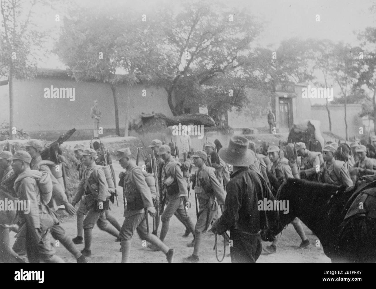 The retreat from Shanghai. Chinese troops march to defend capital. This picture, just received in London, shows Chinese troops, rifles and blanket slung across their shoulders, marching through a village to the North of Shanghai, on their way to help in the defence of Nanking, the capital, which is now threatened by the Japanese. These troops were forced to retreat from Shanghai and hurried nor to reinforce Nanking's defenders 21 November 1937 Stock Photo
