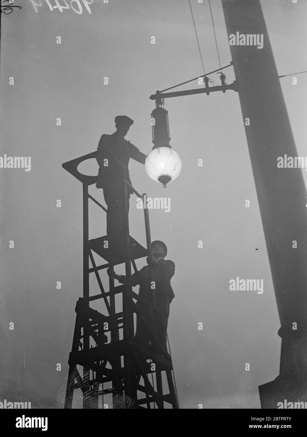 Fog slows down, London. Thousands of Londoners were held up on their way to work by the thick white fog which to lay transport services. Photo shows, workmen silhouetted as they attended a lamp in the foggy gloom at Liverpool Street station. 18 October 1937 Stock Photo