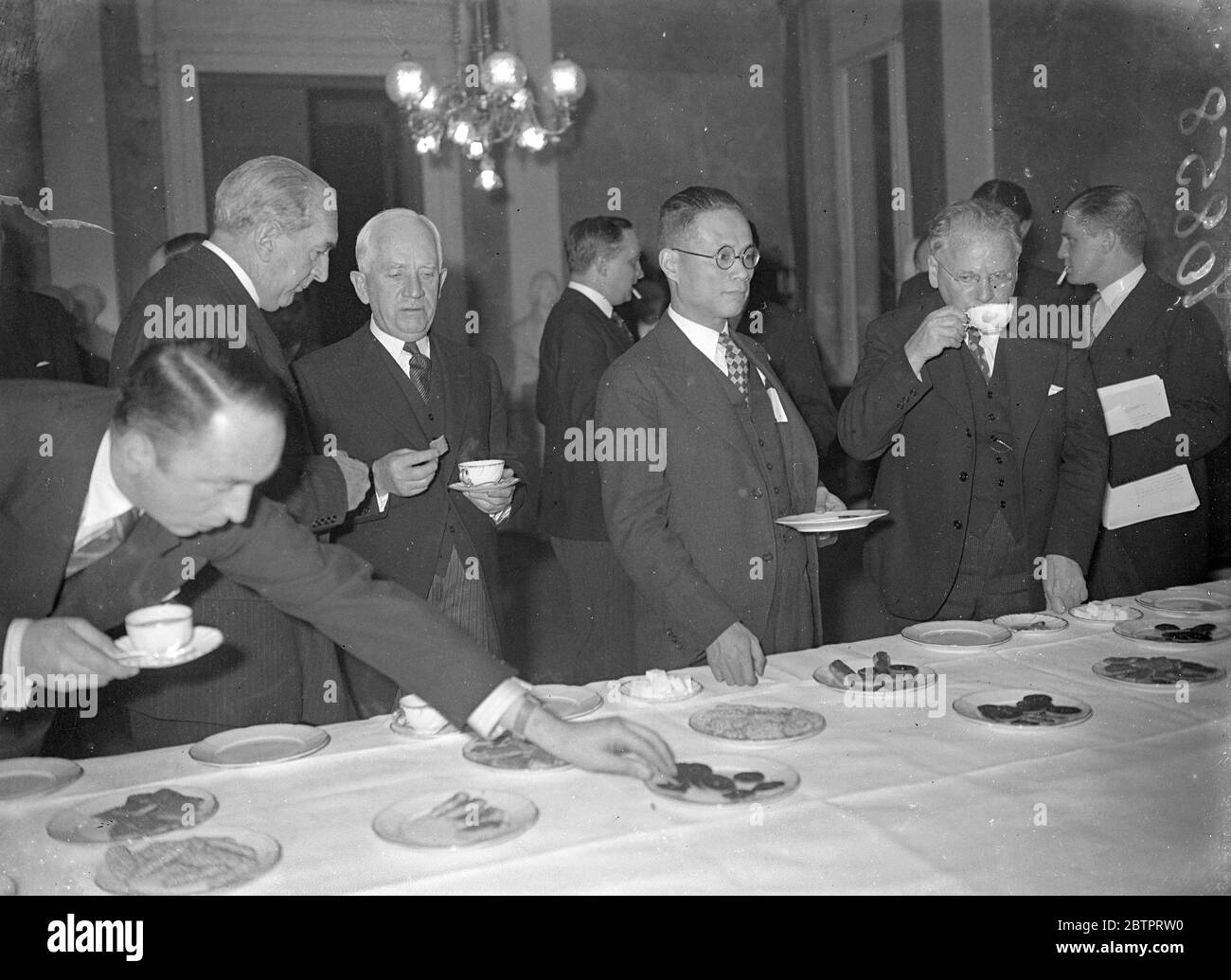 Buffet in Brussels. Far East conference delegates take refreshment. Tea and biscuits for delegates to the Nine Power Conference on the Far East War in Brussels. On left (profile) is Mr S M Bruce, the Australian delegate, who is in conversation with Mr Norman Davis, the American representative. Extreme right, intent on his teacup, is Mr Maxim Litvinoff, Soviet delegate. 4 November 1937 Stock Photo