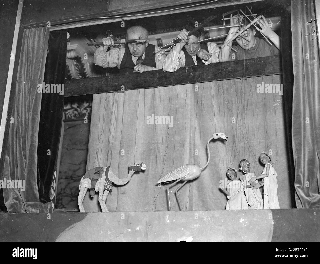 Pulling the strings!. Puppet show opens in London. The British Puppet and Model Theatre Guild's twelfth exhibition has opened at a Victory House, Leicester Square. The exhibition includes puppets, shadows, marionettes, scenic designs and model stages. Photo shows, exhibitors manipulating their puppet on a model stage. 25 October 1937 Stock Photo