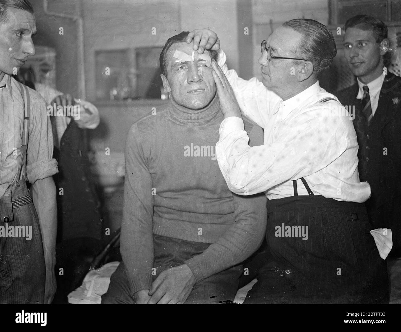The fruits of victory!. Eddie Phillips has plaster over both eyes. Despite cuts over both eyes, Eddie Phillips, the London heavyweight, scored a points victory over Arno Kolblin, champion of Germany and Europe, in a 12 rounds contest at the Harringay Arena, London. Photo shows, Eddie Phillips cut eyes being liberally bedecked with sticking plaster by his manager, Sam Russell, after the fight. 4 November 1937 Stock Photo