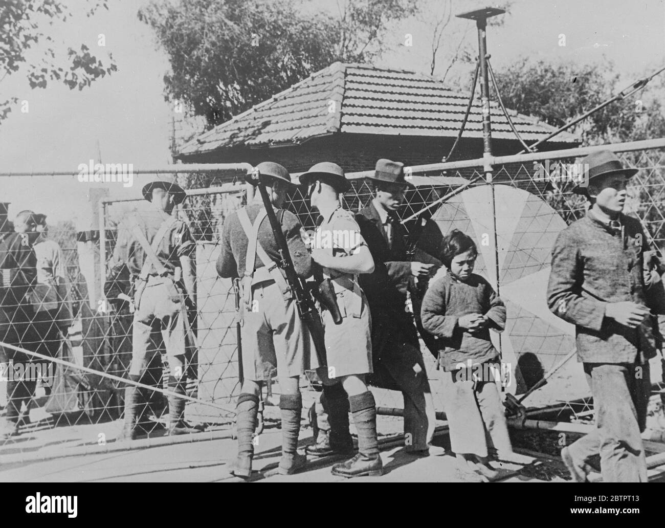 The Ulsters let them through. Chinese refugees, including a tearful little girl with clasped hands, passing into the international settlement at Keswick and Great Western Roads, Shanghai, after examination for weapons by men of the Royal Ulster rifles. 23 November 1937 Stock Photo