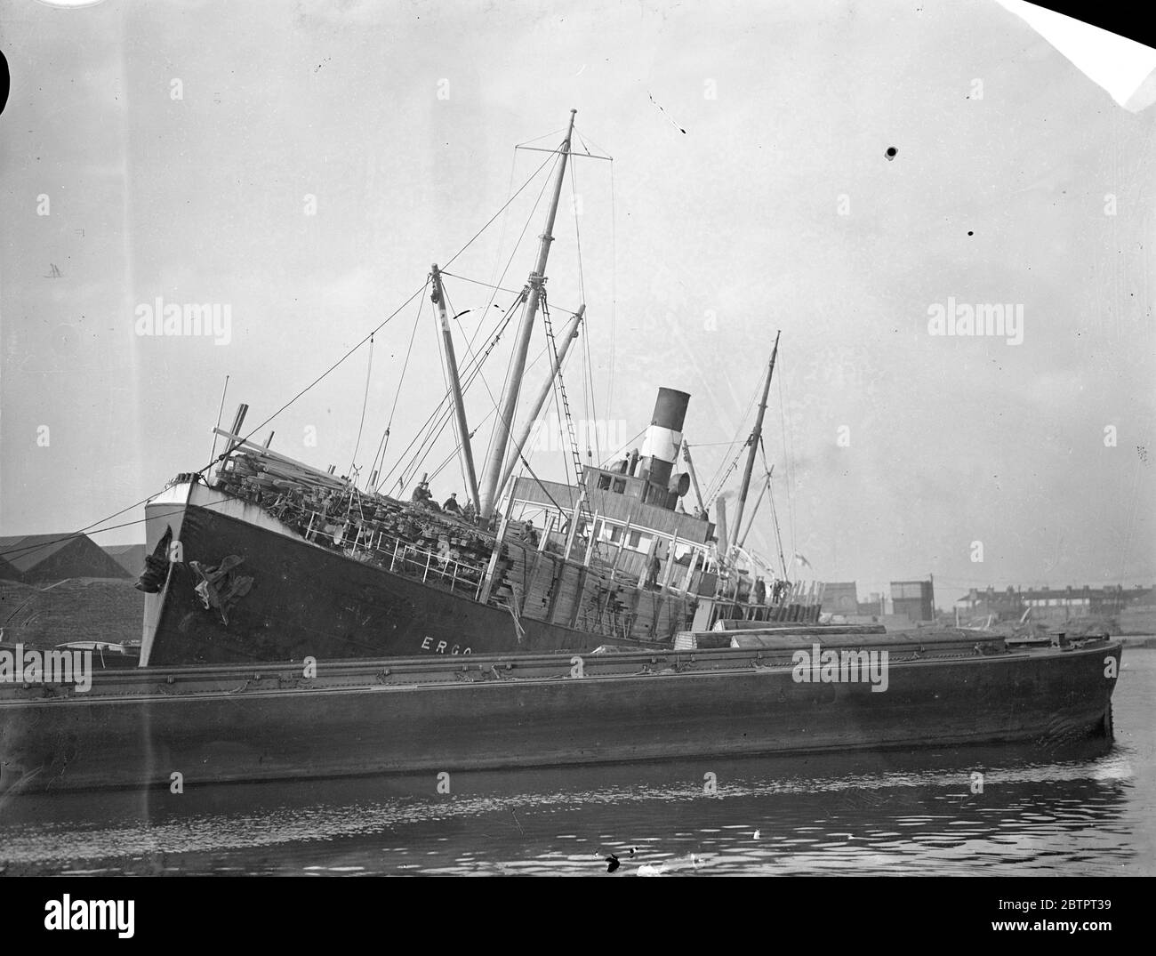 Import with a heavy list. Finnish steamer supported by barges in Surrey docks. Making her way up river with a heavy list, the Finnish timber steamer 'Ergo' reached the Surrey commercial docks, London, and had to be supported by barges. She was carrying a deck cargo of timber.. 28 October 1937 Stock Photo