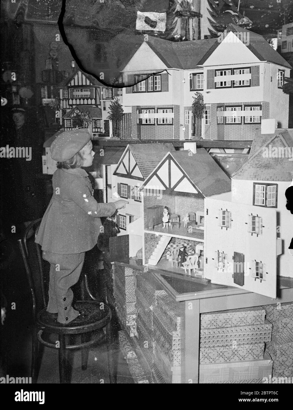 Dream come true!. Standing tiptoe on a convenient chair, this small visitor eagerly chooses her dolls house from the Christmas fair at Gamages, in Holborn. 19 November 1937 Stock Photo