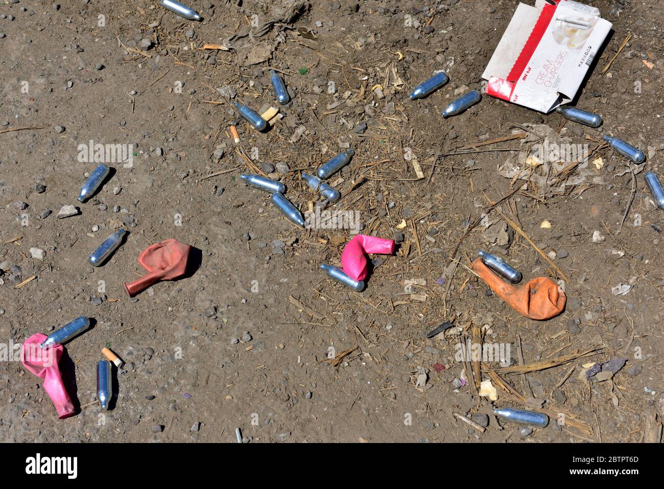 Discarded nitrous oxide (laughing gas) canisters and balloons littering ground Stock Photo