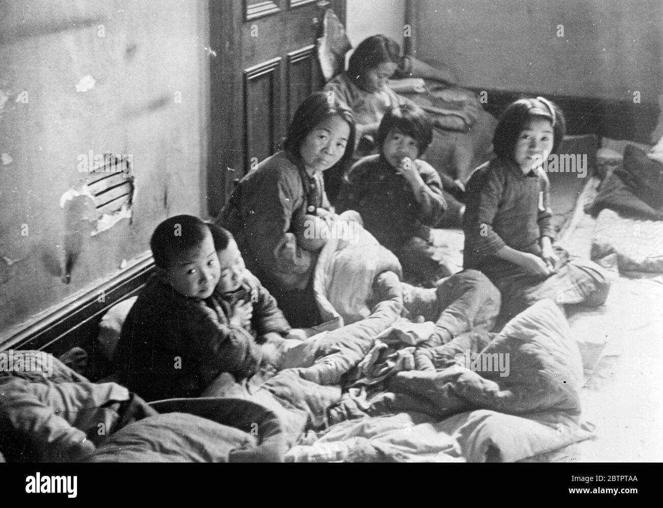 Christmas comes to China. A Chinese family, huddled together for warmth beneath the few blankets and rugs salvaged from their bombed time, Crouch, despondent in the corner of a room at Shanghai refugee camp. Although the Christmas season approaches this family, like many in the China war zones, knows nothing of goodwill. A few handfuls of rice forms their meagre rations. Japanese armoured cars had taken the place of Father Christmas and his slaves. 19 December 1937 Stock Photo
