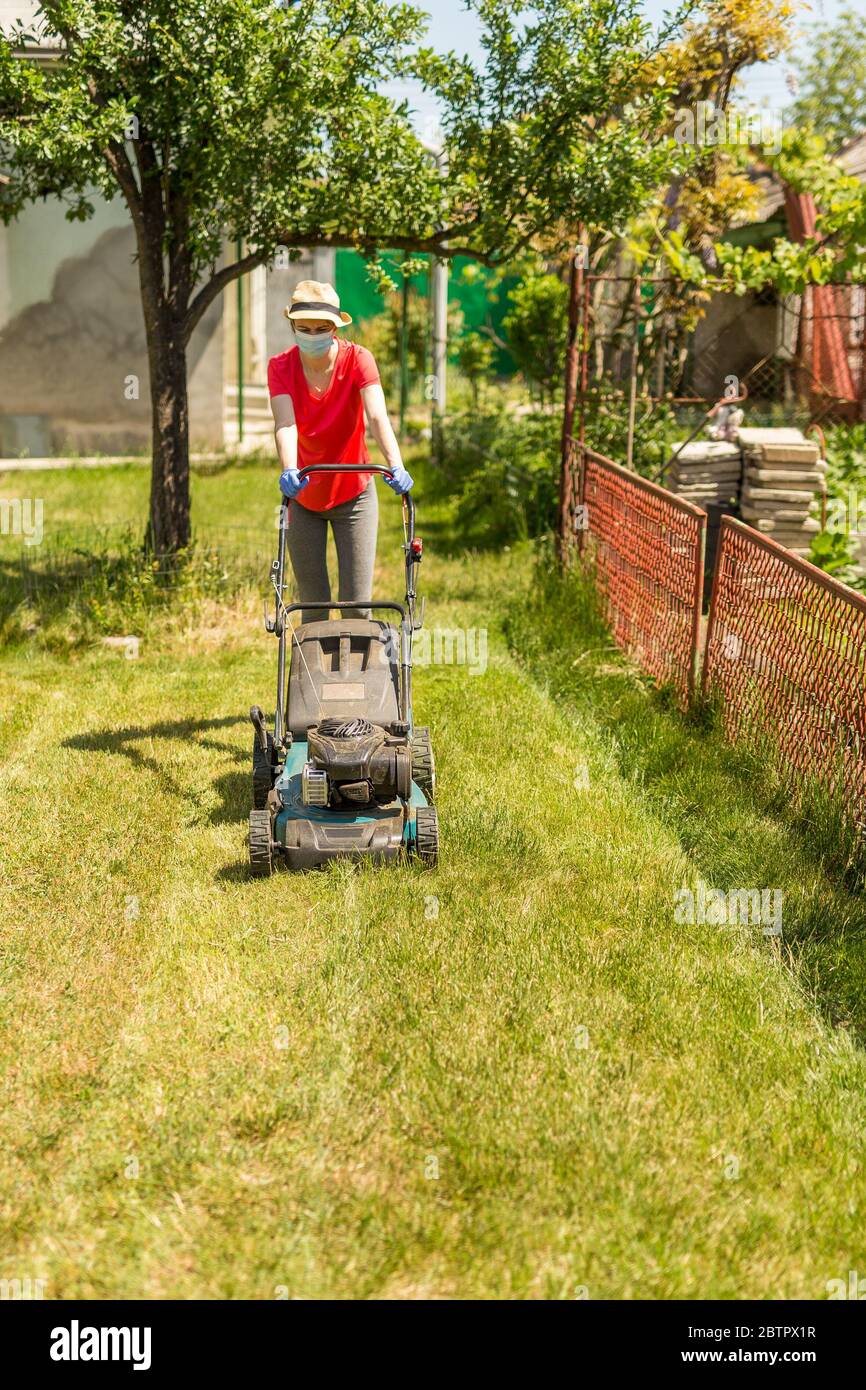 A woman in her backyard mowing grass with a lawn mower on a sunny day at  home wearing a surgical mask because of the coronavirus epidemic Stock  Photo - Alamy
